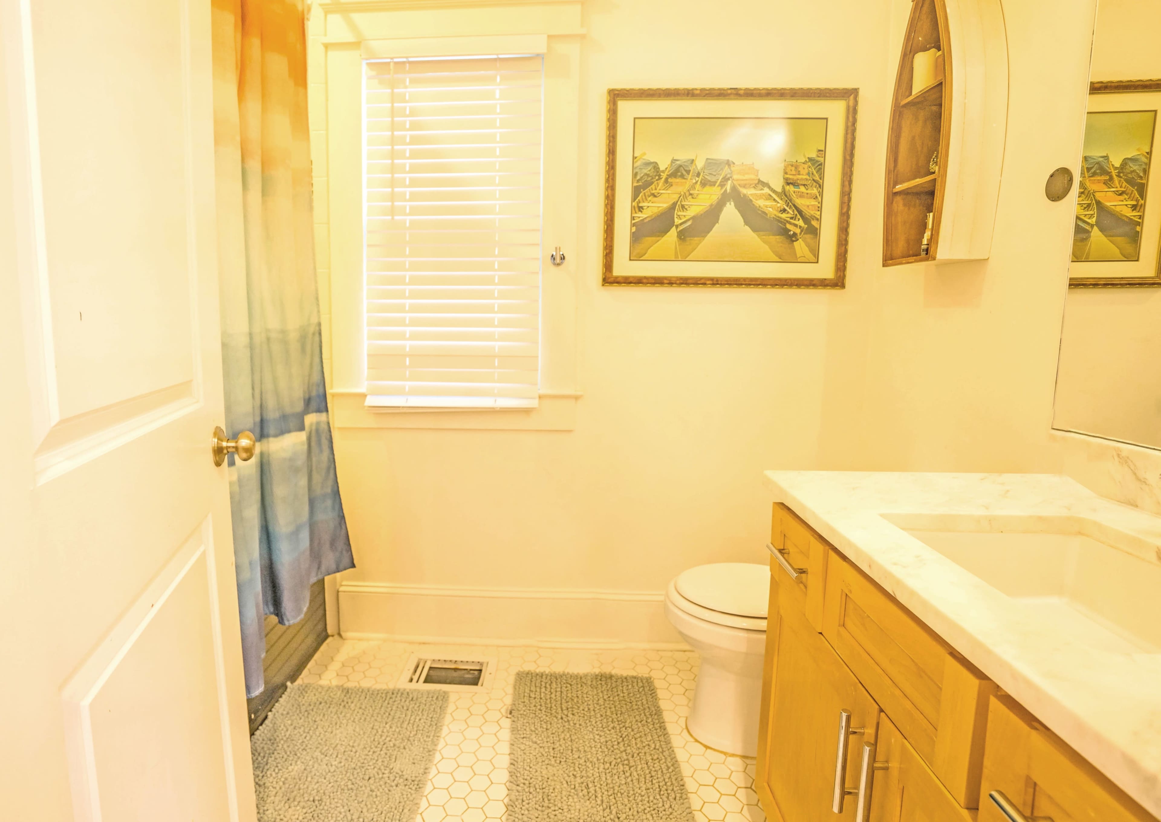 A bathroom with a colorful shower curtain, a white toilet, a marble countertop sink, and a framed artwork on the wall.