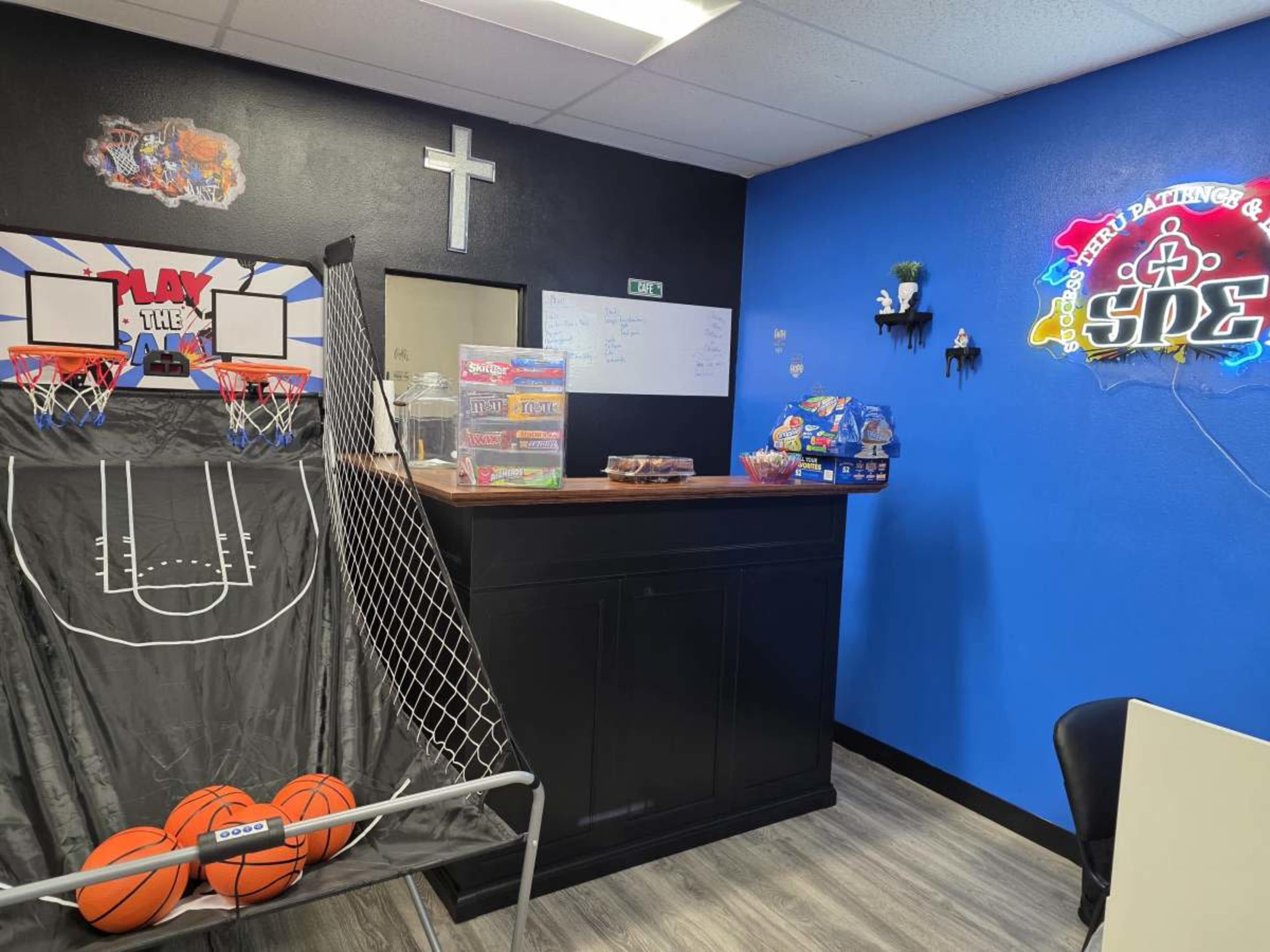 The image shows a recreational area with a basketball shooting game, a counter, and colorful wall decorations in a room with blue and black walls.