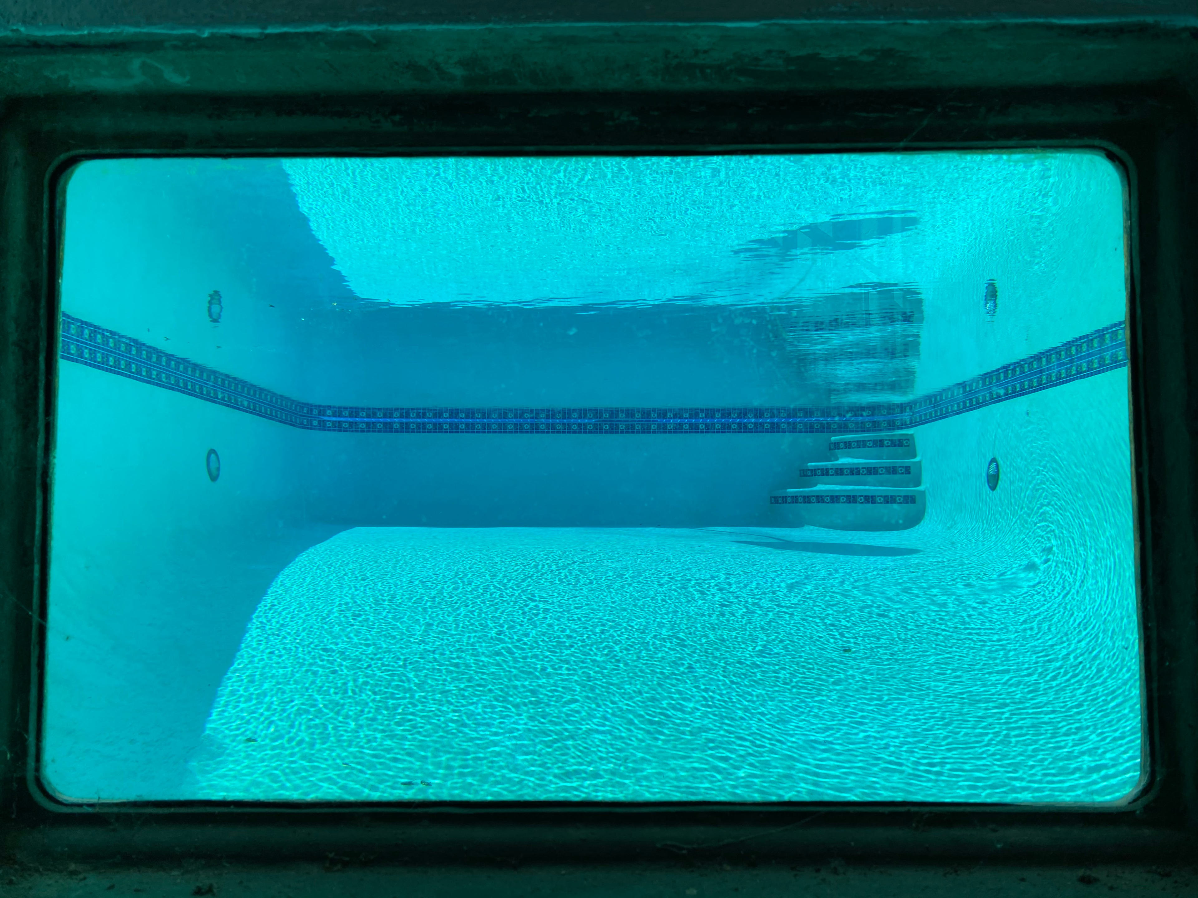 The underwater view of an empty swimming pool, featuring a tiled border and a set of stairs.