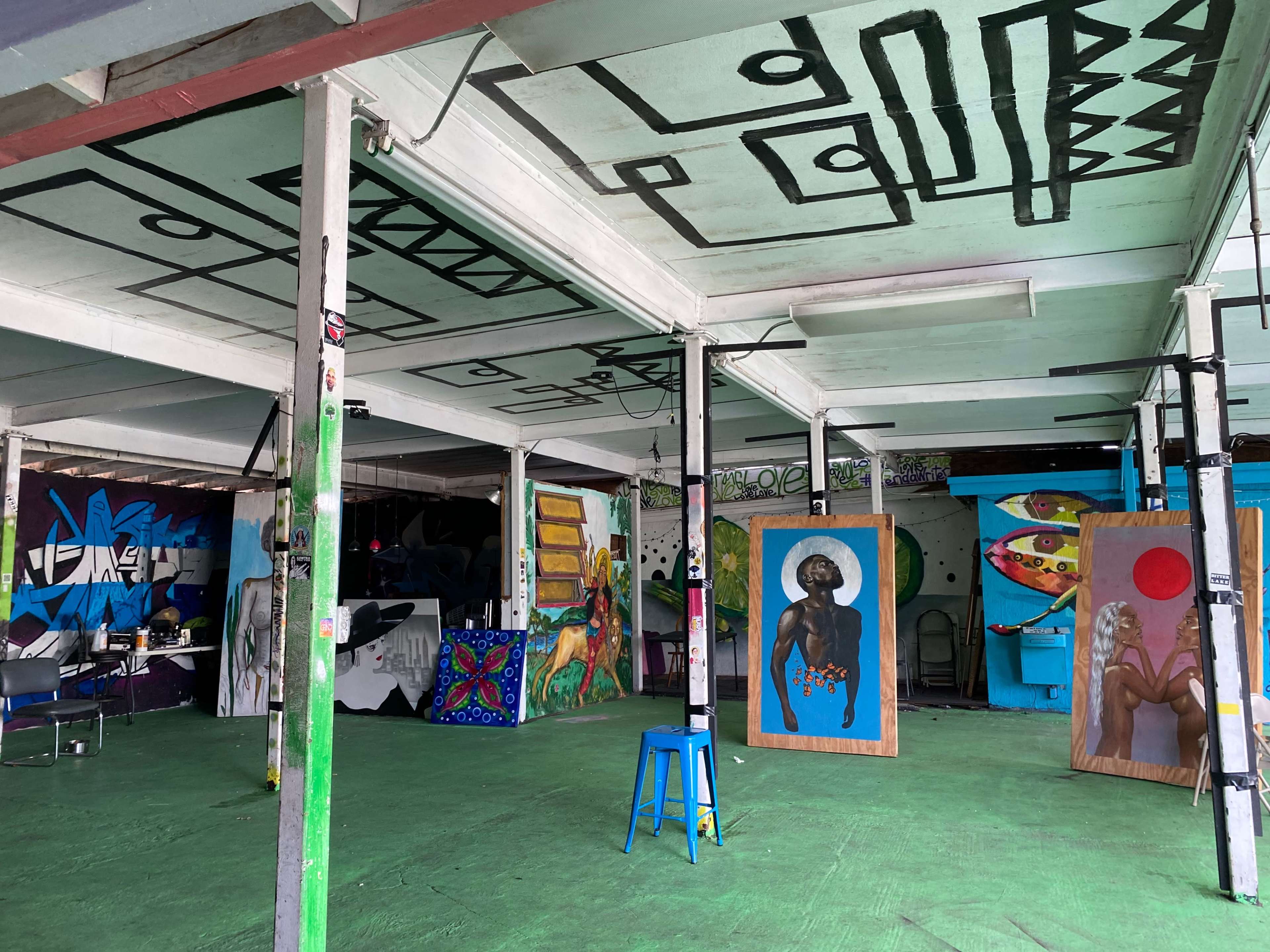 A spacious art studio with various colorful murals and paintings on the walls and a green floor.