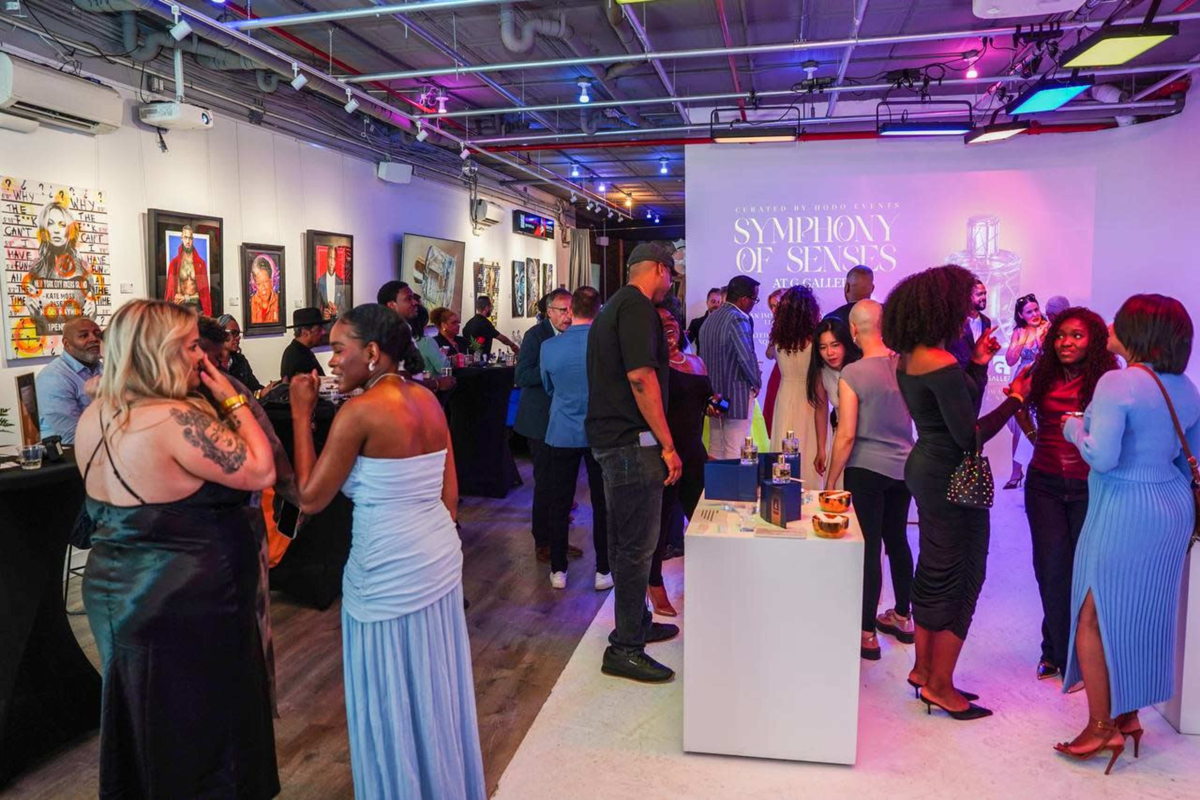 A diverse group of people mingles at a gallery event featuring artwork and a display for a fragrance called "Symphony of Senses."