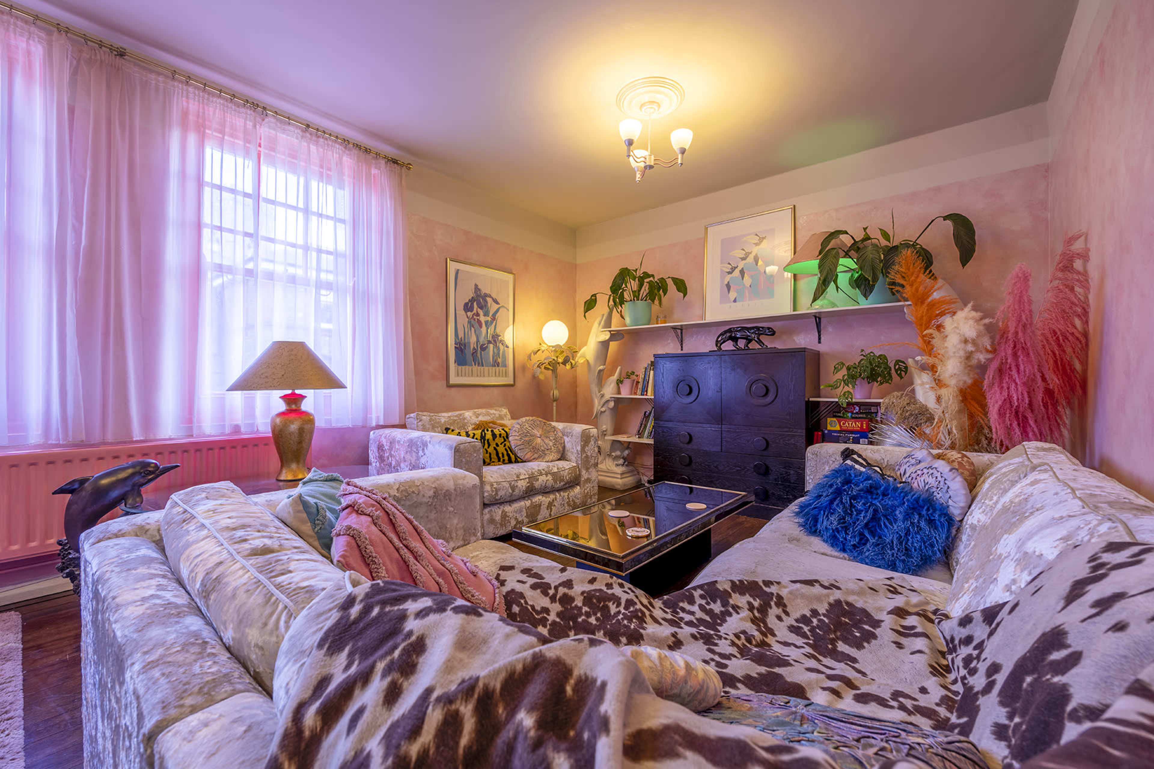 A cozy living room with plush, patterned sofas, a coffee table, and various houseplants under soft lighting.