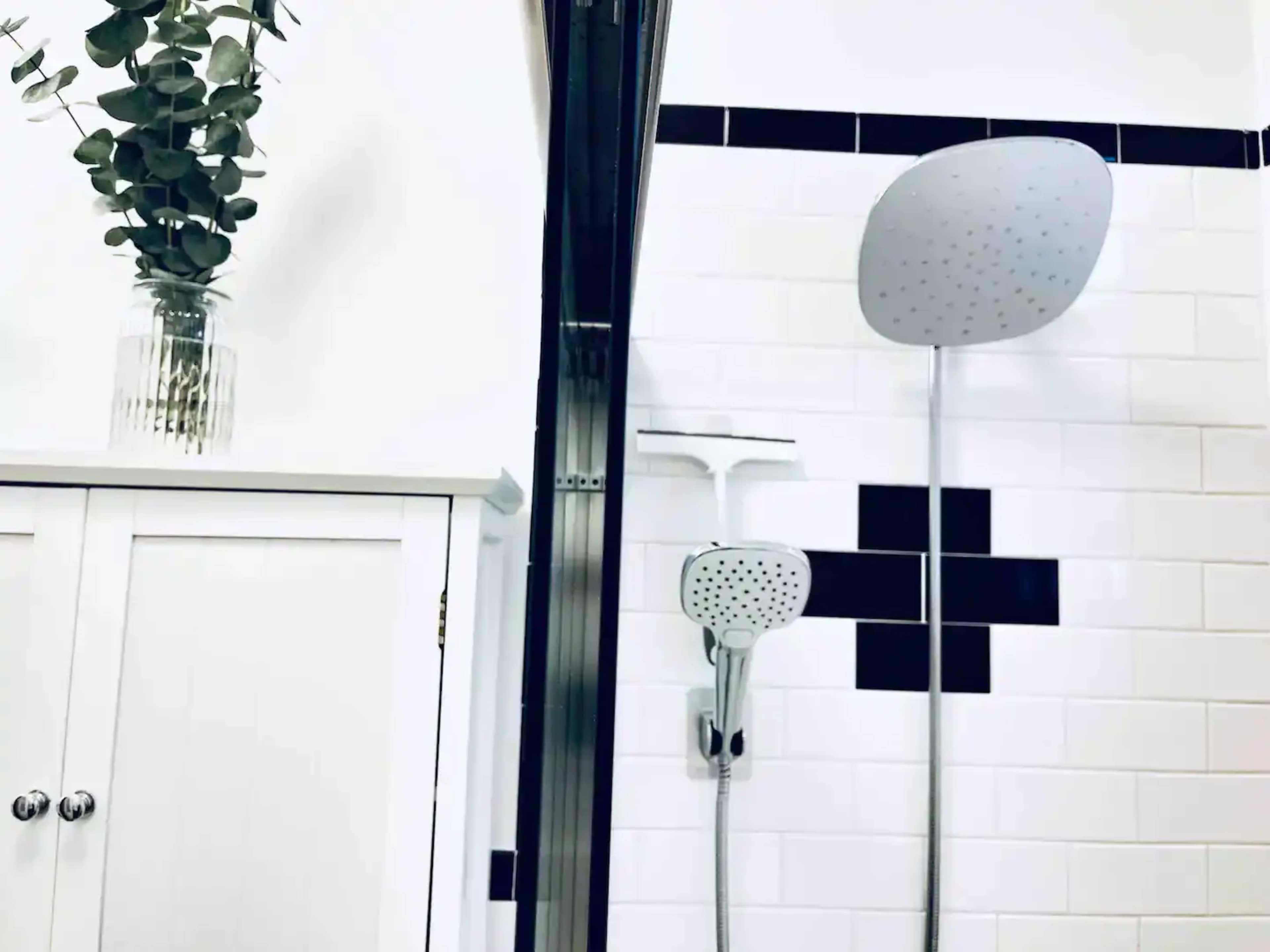 A modern bathroom featuring a showerhead, a handheld shower attachment, and a cabinet beneath a decorative plant in a vase.