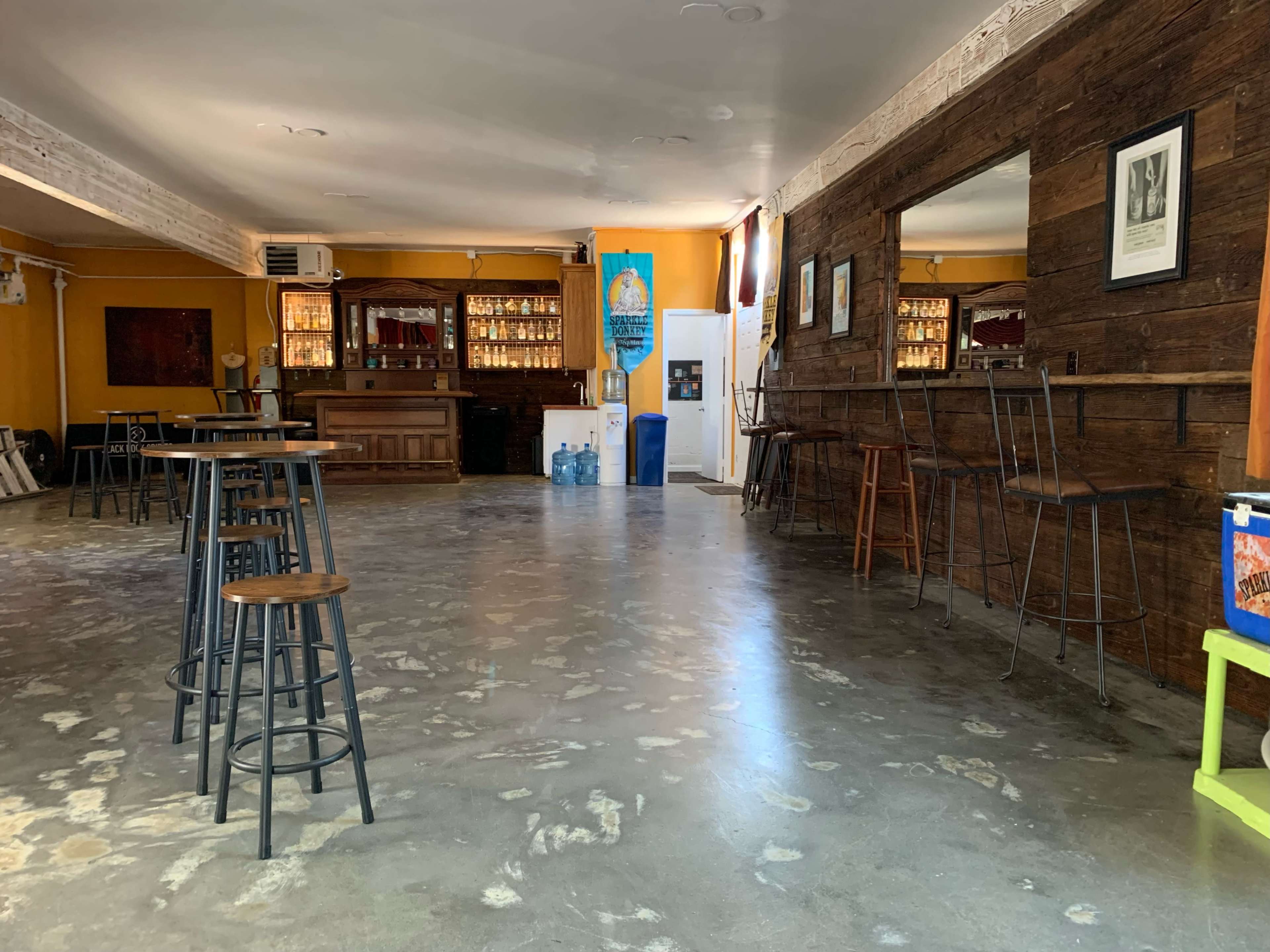 A spacious bar area with wooden walls, a bar counter in the background, and several high stools positioned around the room.