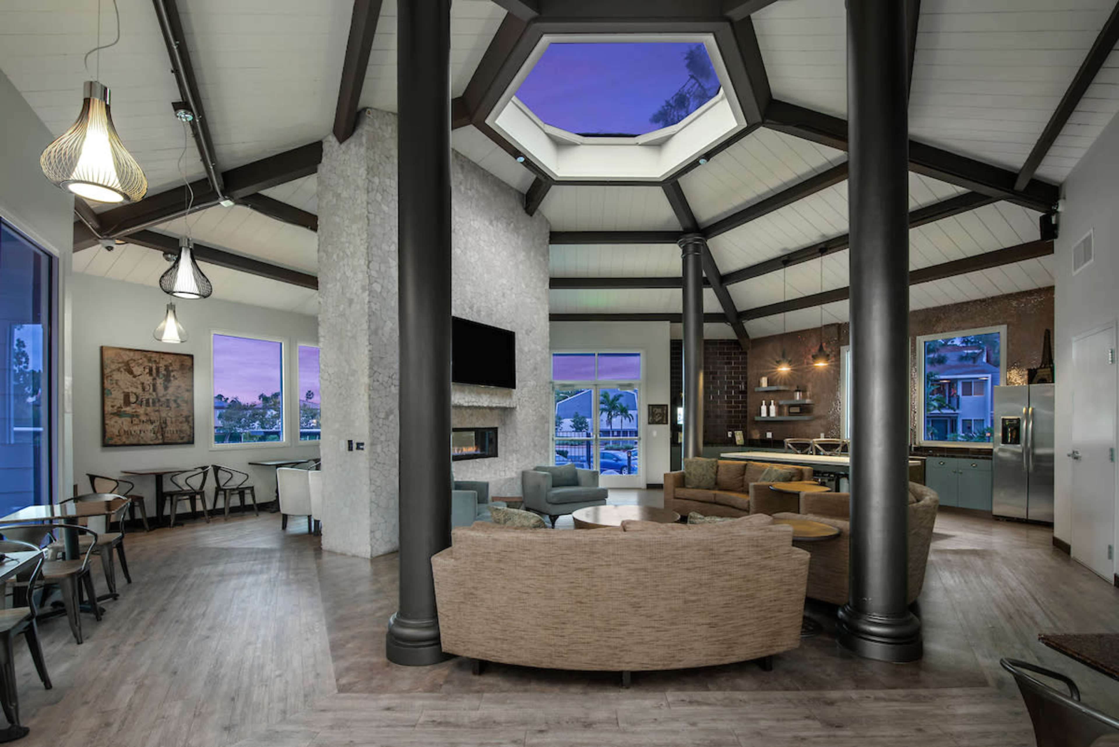 A modern living space with a high, octagonal ceiling, large windows, and a mix of seating arrangements around a central area with a fireplace.