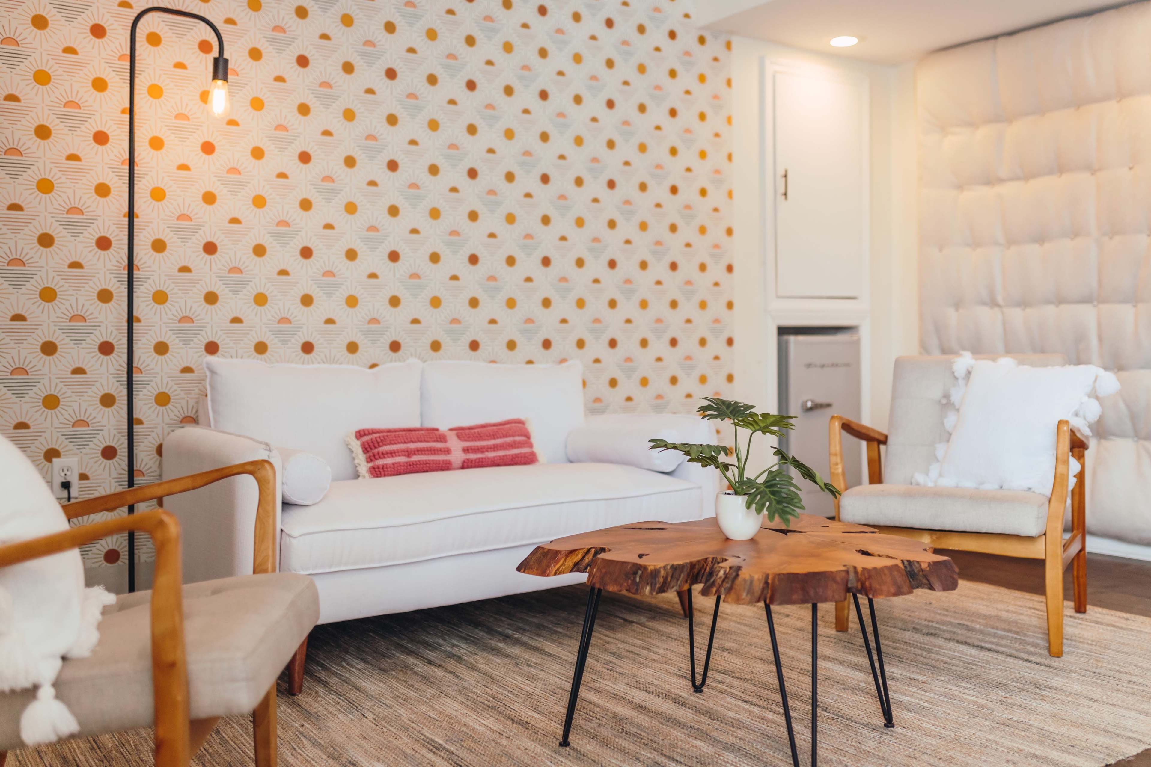 The scene features a modern living room with a white sofa, a wooden coffee table, and patterned wallpaper.