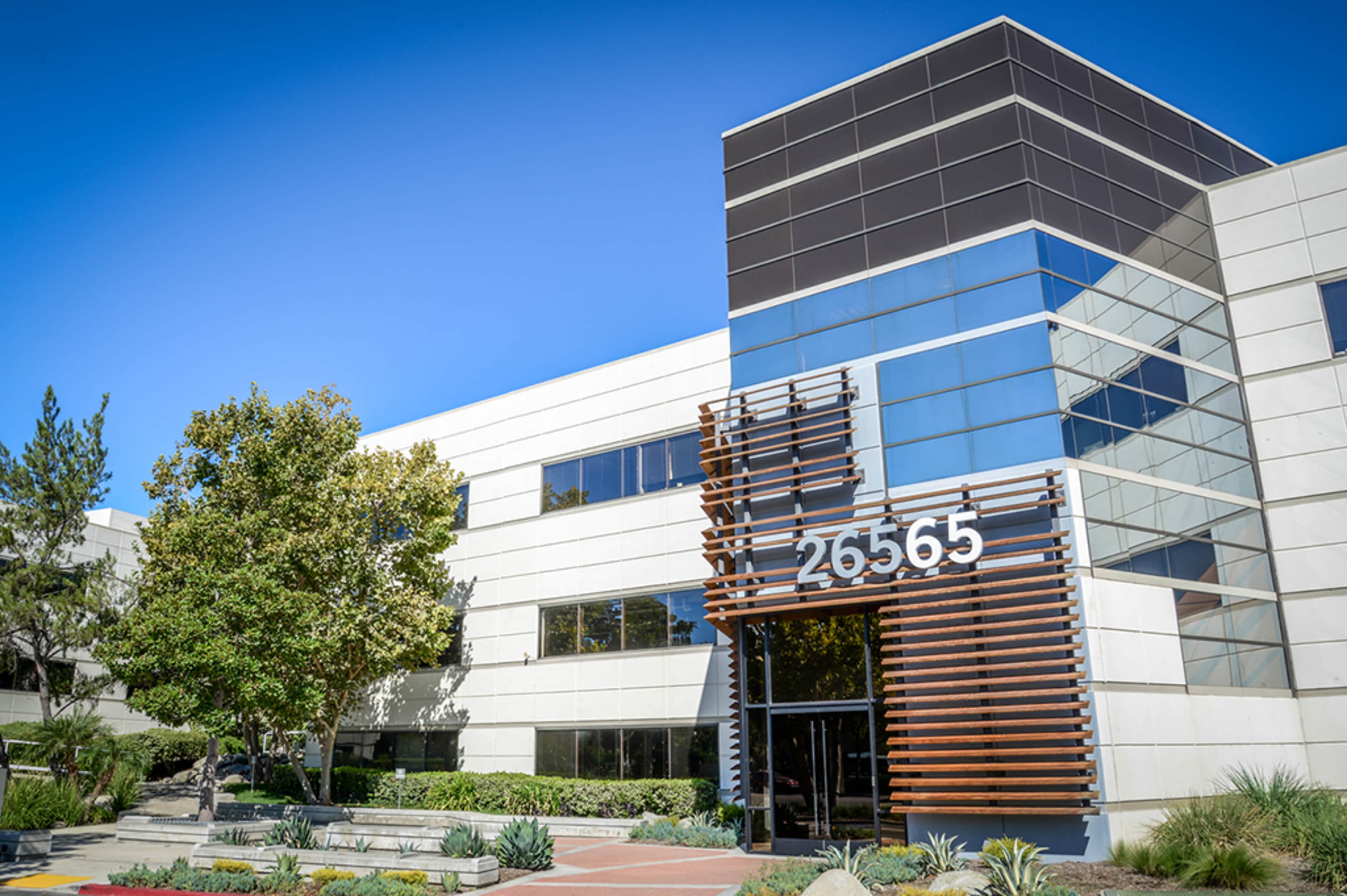 A modern office building with large glass windows and a prominently displayed address of 26565 at the entrance.