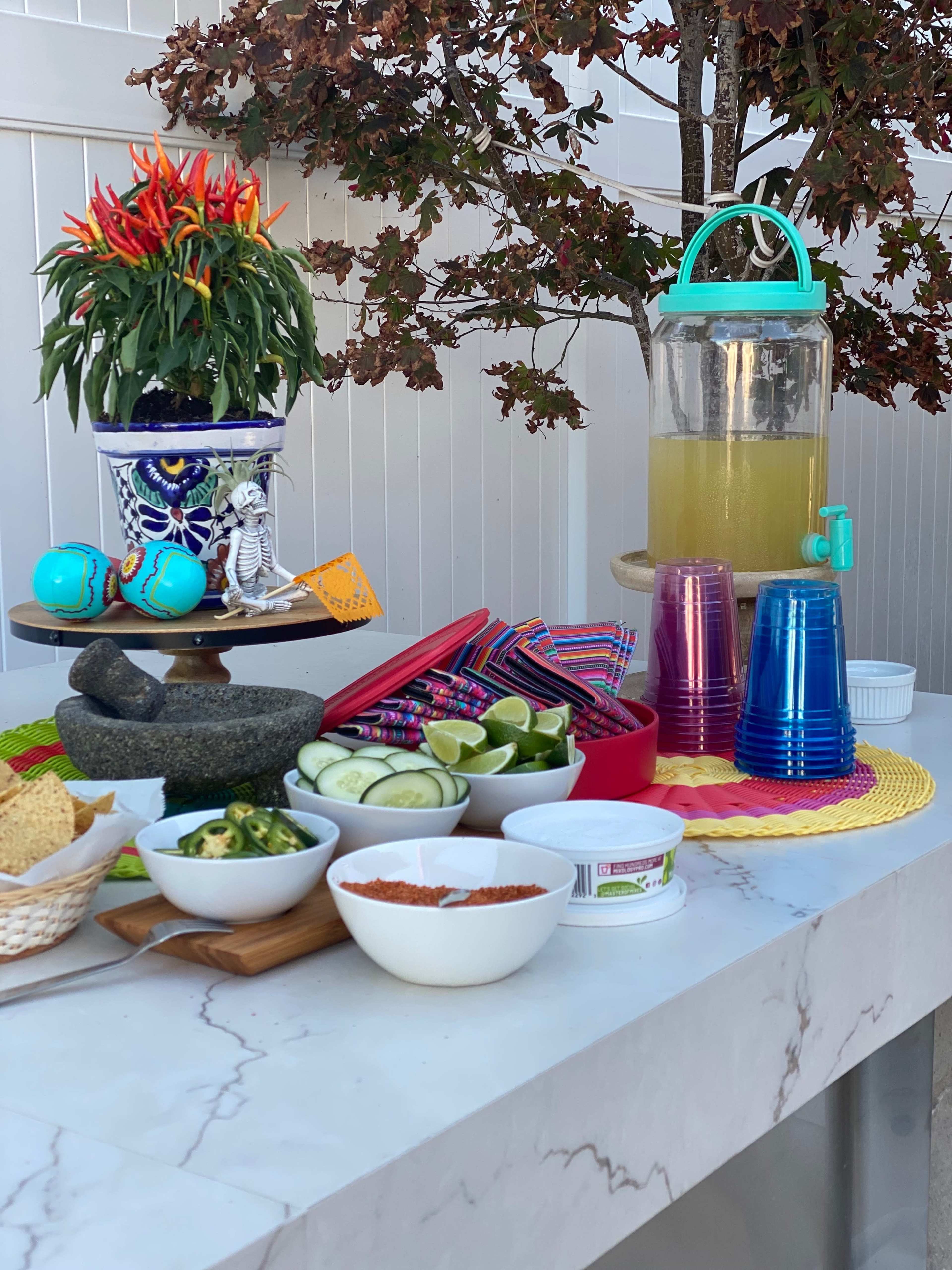 A vibrant outdoor food and drink setup featuring a variety of dishes, beverages, and colorful decorations on a marble tabletop.