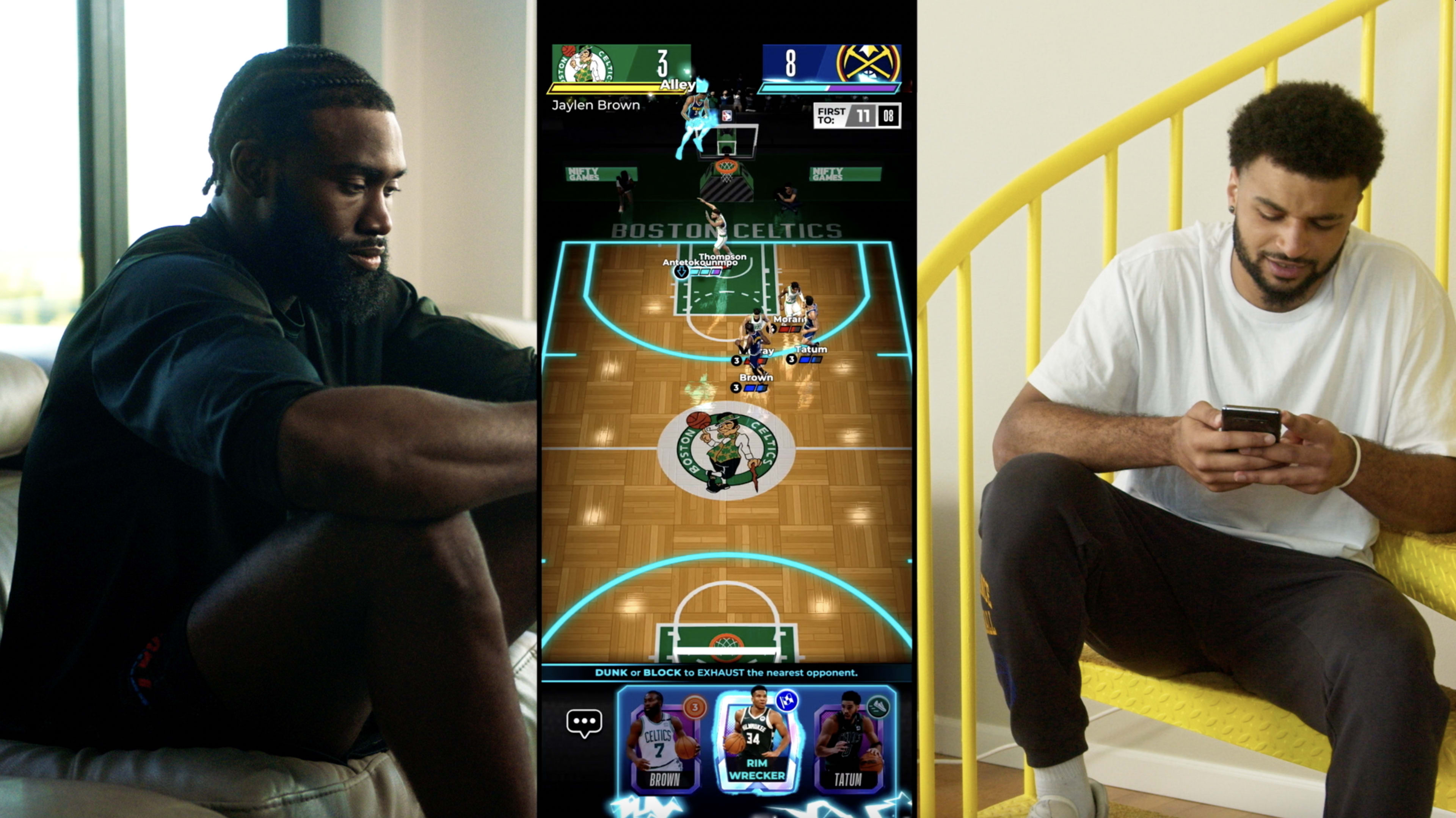A man sits on a couch observing a basketball video game on a screen, while another man, seated nearby, looks at his phone.
