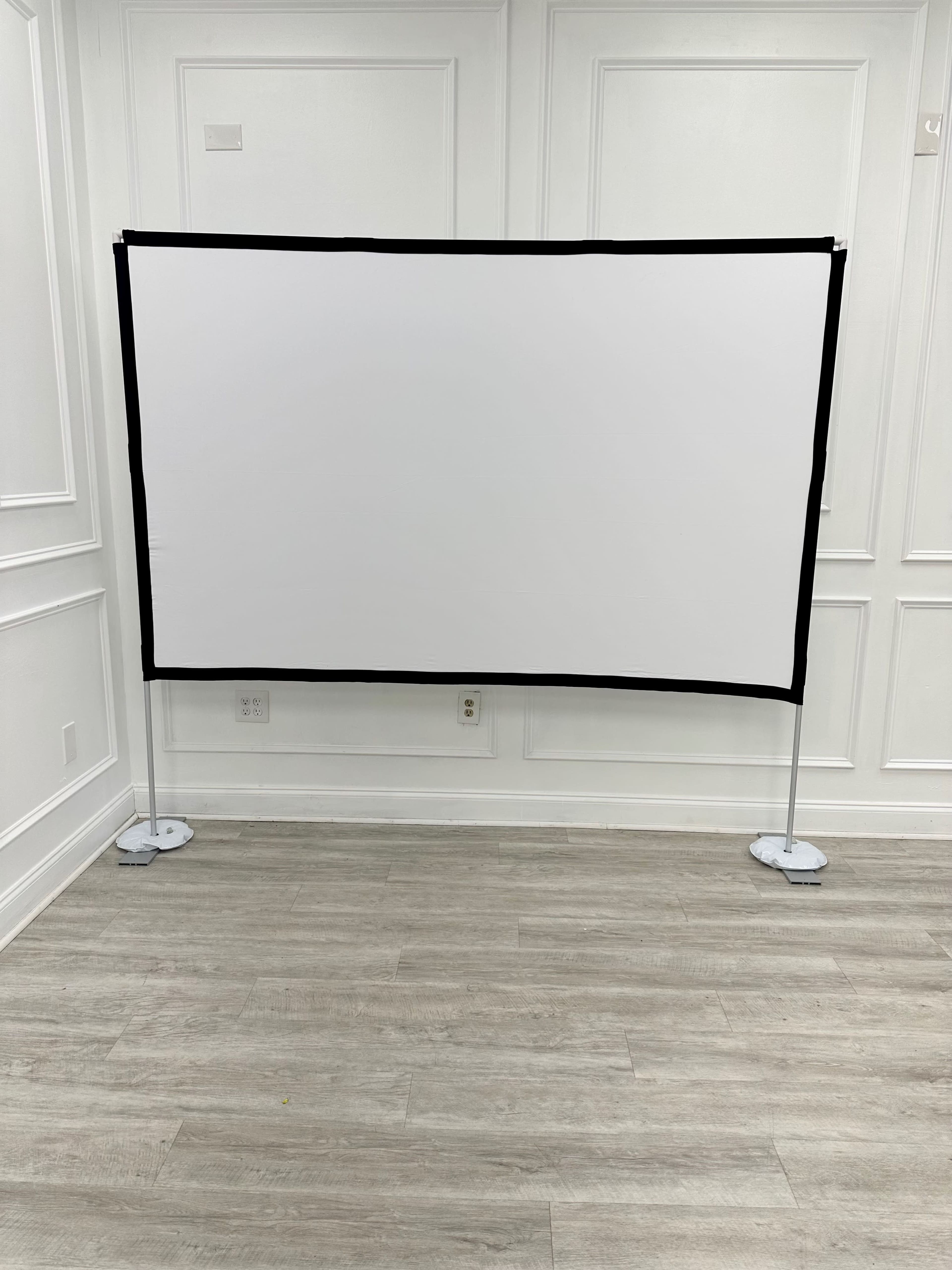 A blank projection screen stands on a tiled floor against a plain white wall.
