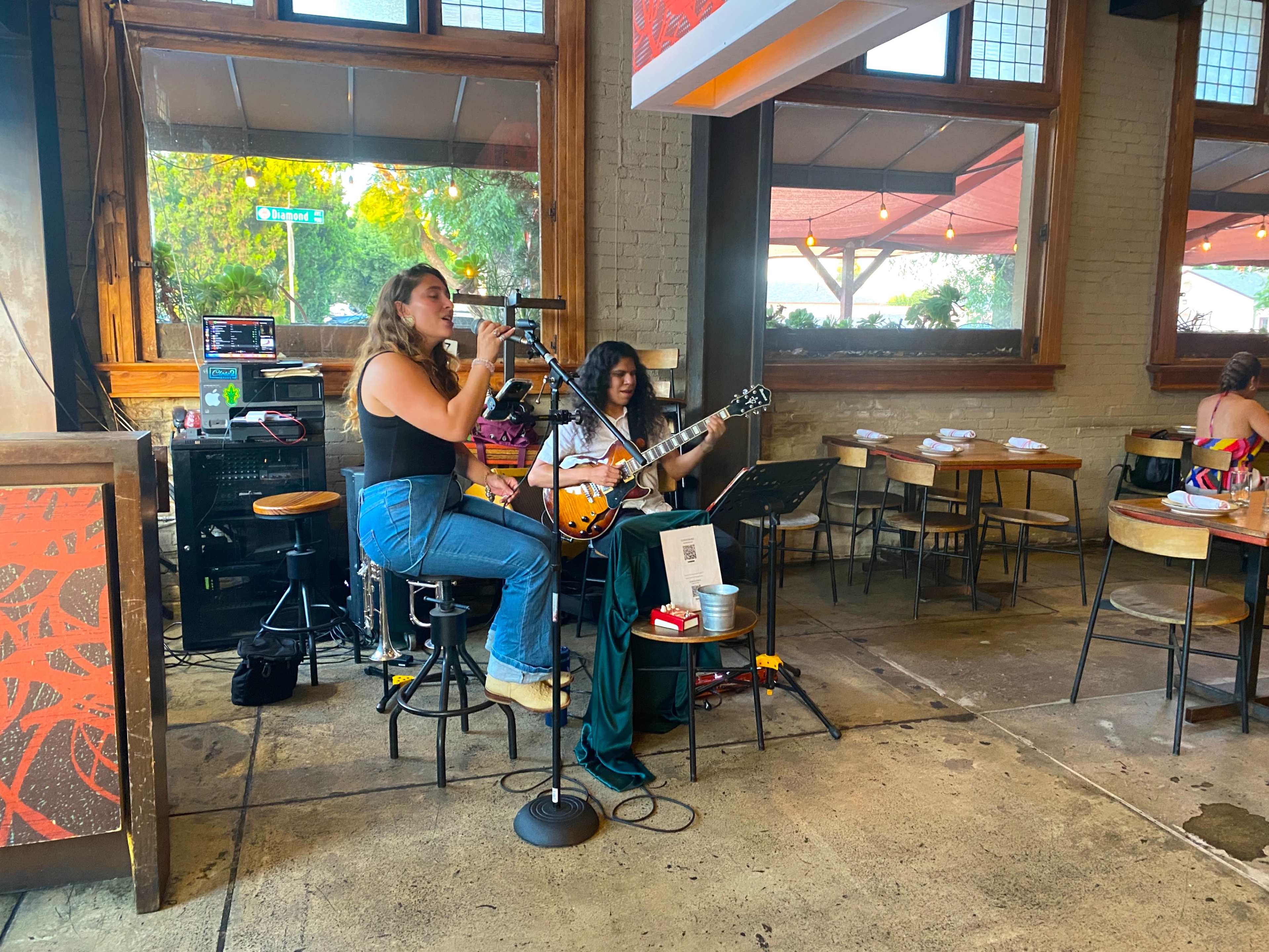 Two musicians perform live music in a spacious restaurant, with one singing and the other playing guitar.
