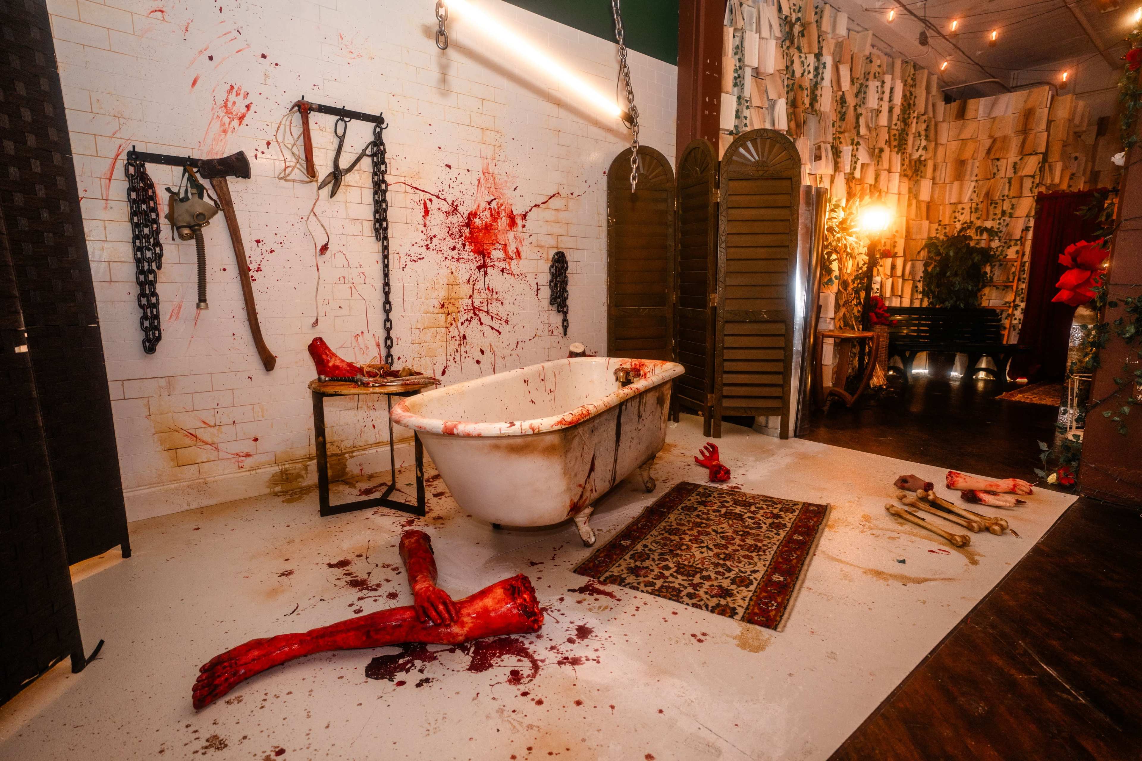 The scene depicts a dimly lit room featuring a vintage bathtub surrounded by gruesome props, including severed limbs and blood splatter on the walls.