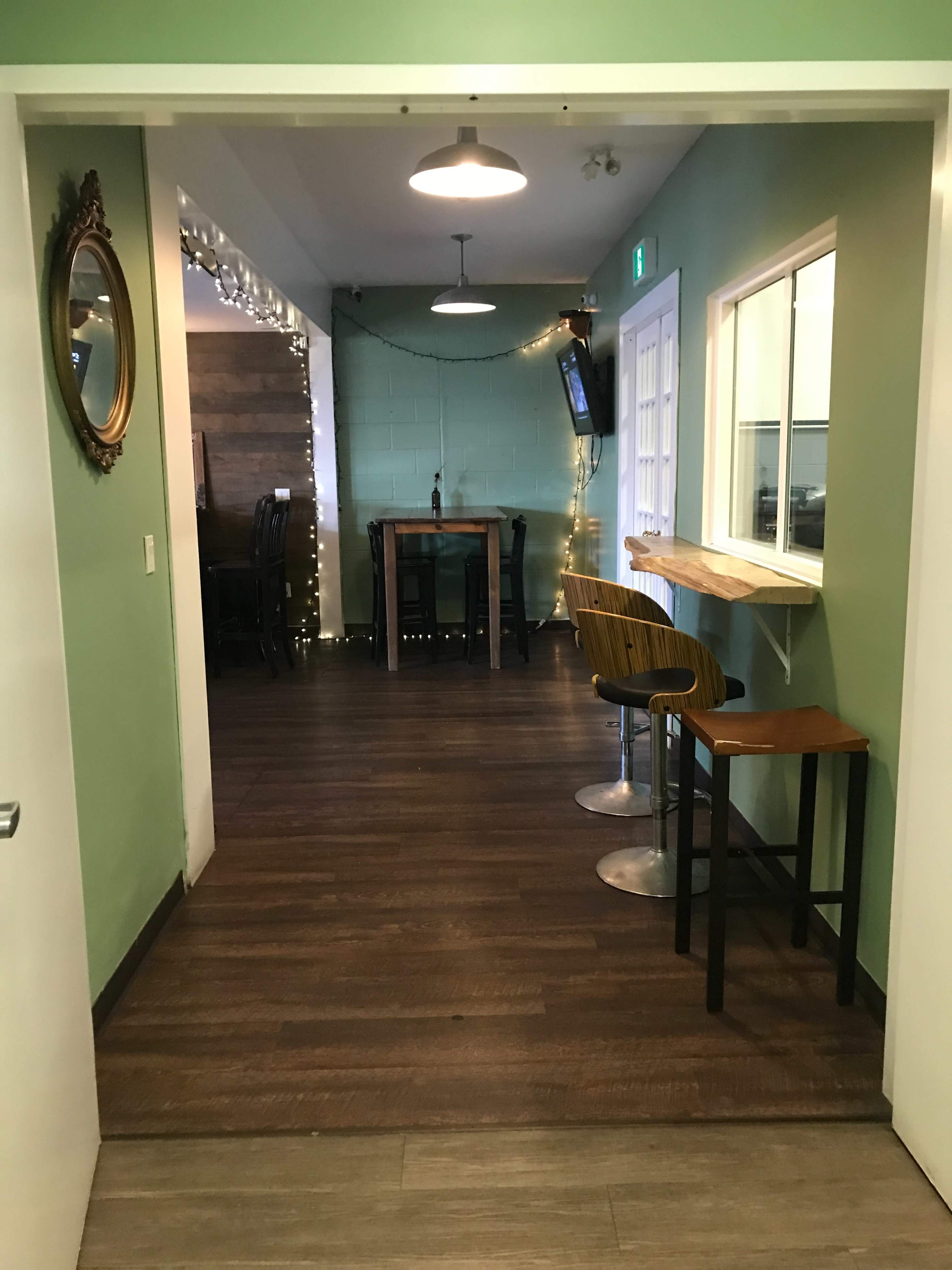 A hallway leading to a dining area with green walls, wooden flooring, and bar stools at a counter.