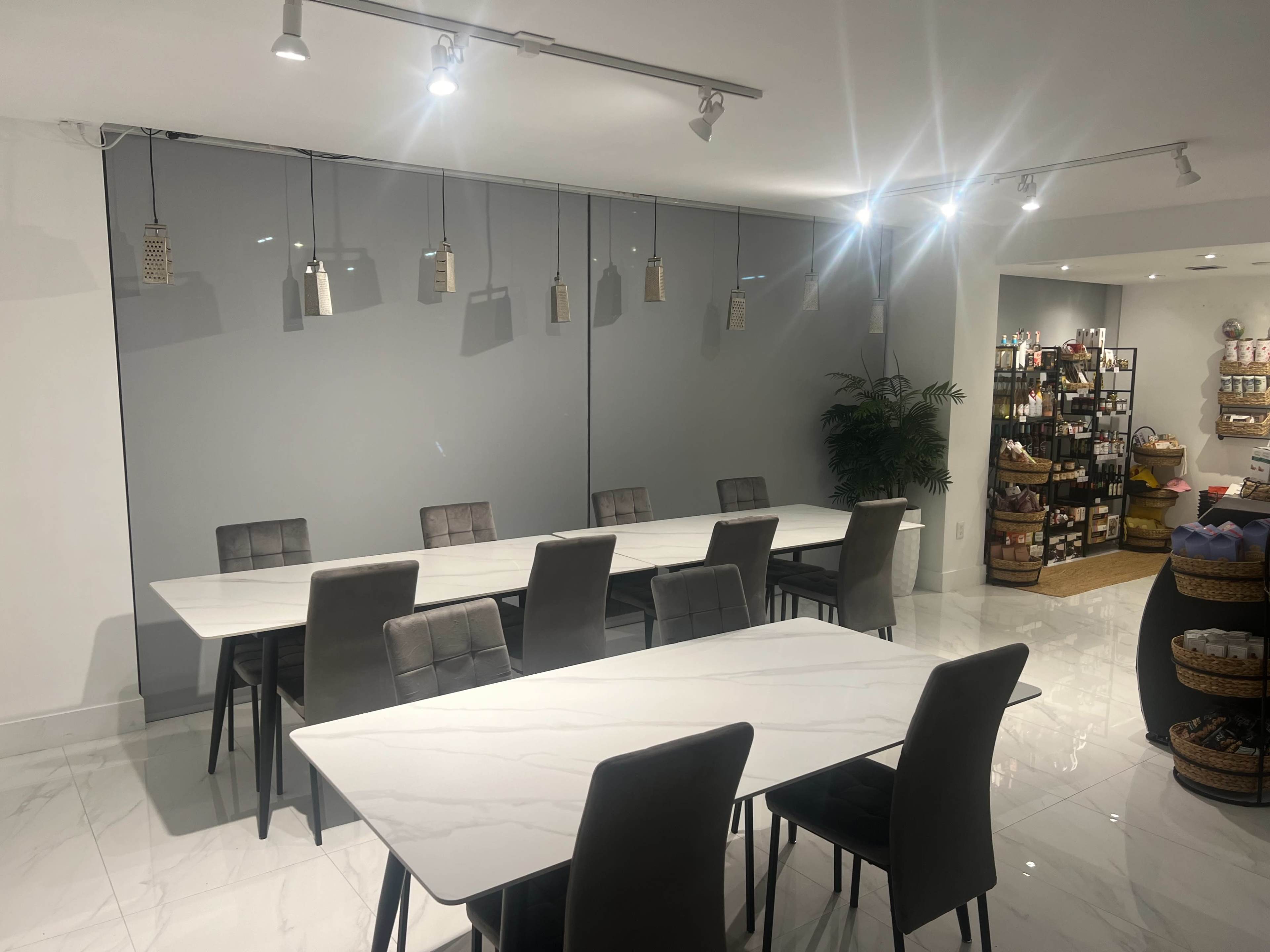 A modern conference room features two large marble tables surrounded by gray chairs, with pendant lights hanging from the ceiling and a retail display visible in the background.