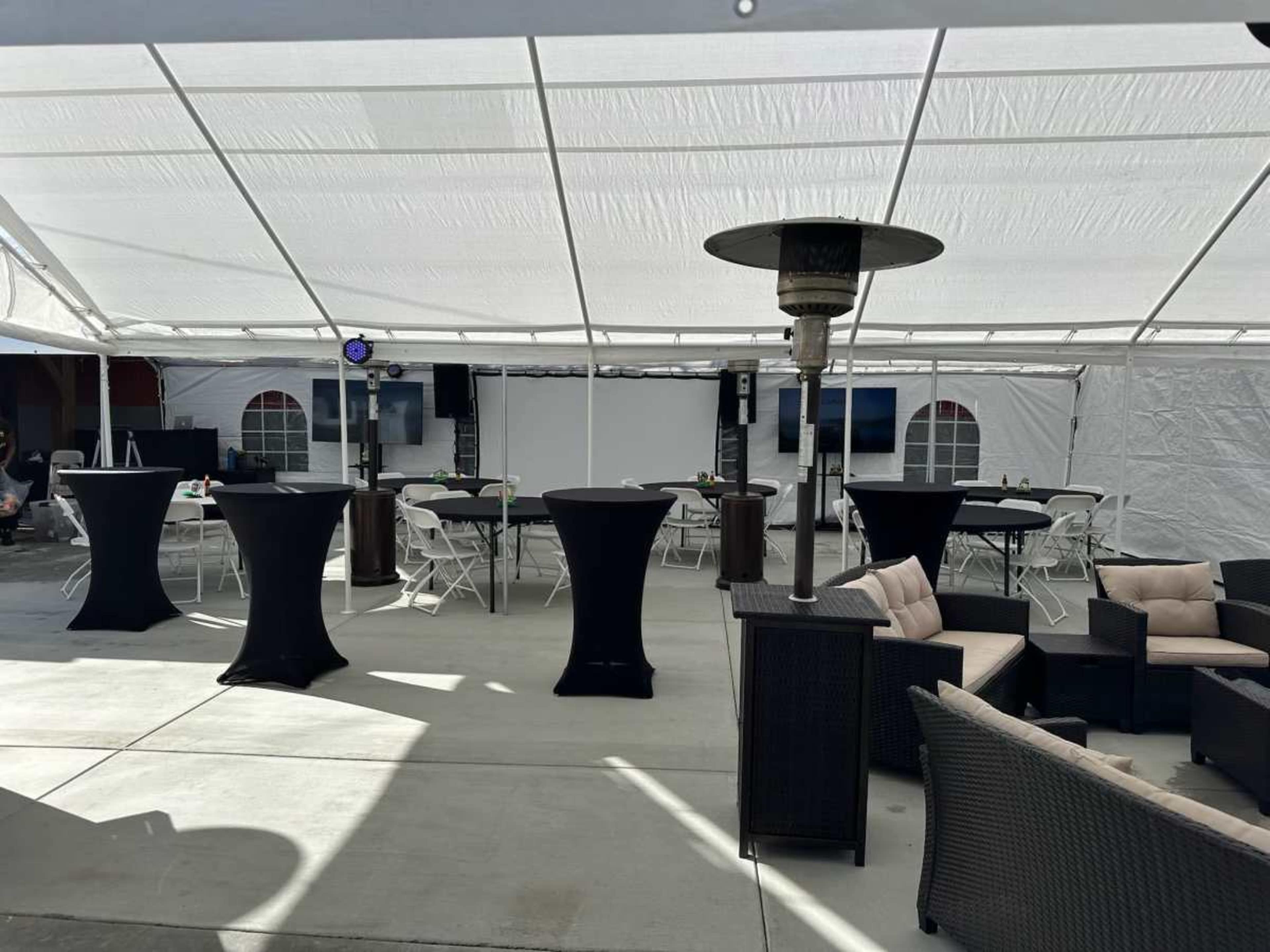 A spacious tent is set up with high-top tables, heating lamps, a large screen at the front, and seating areas arranged in a casual layout.