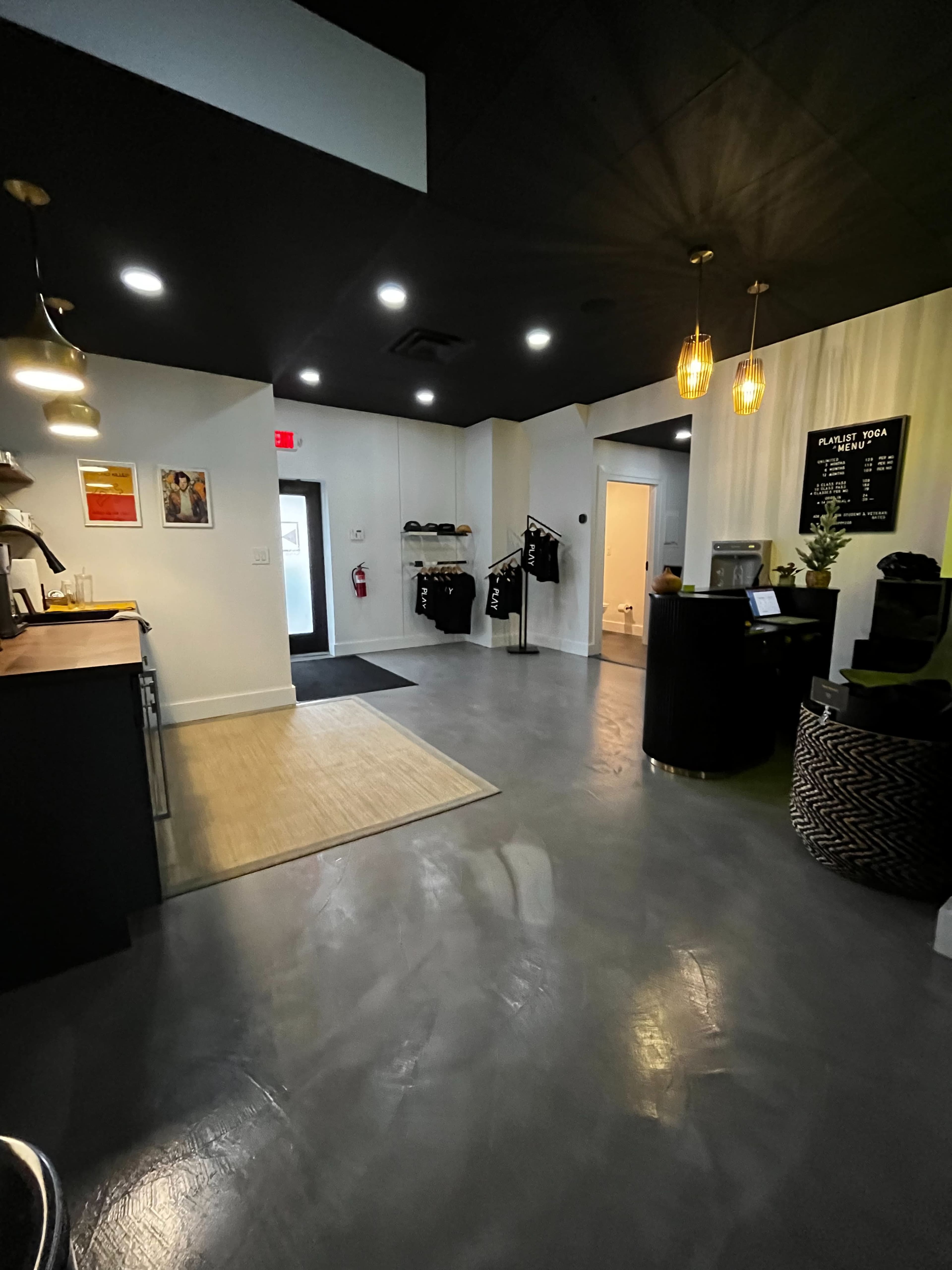A modern reception area of a yoga studio, featuring a black front desk, seating, and a light-colored entryway.