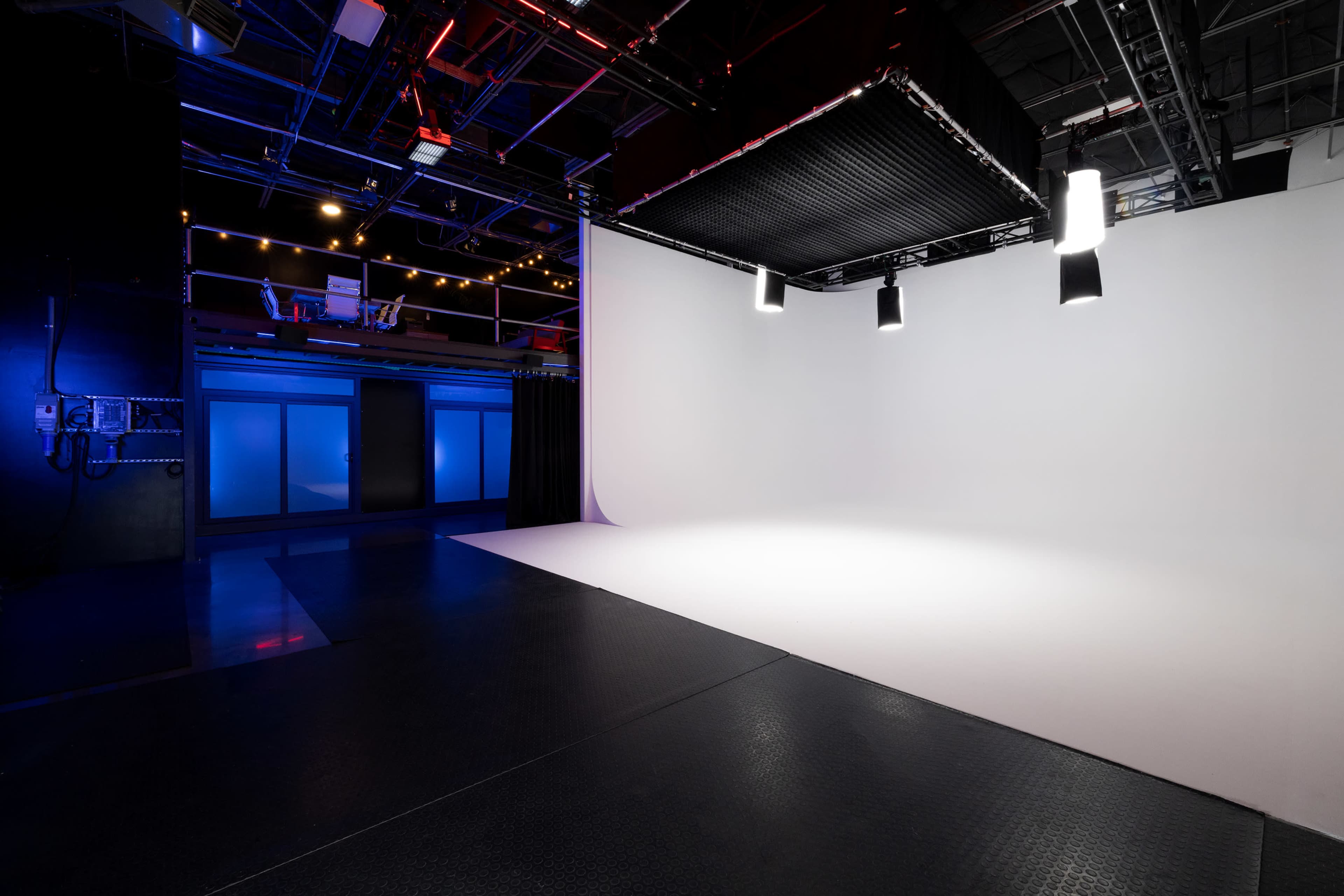 The image shows a spacious studio with a white backdrop, overhead lighting, and a black floor.