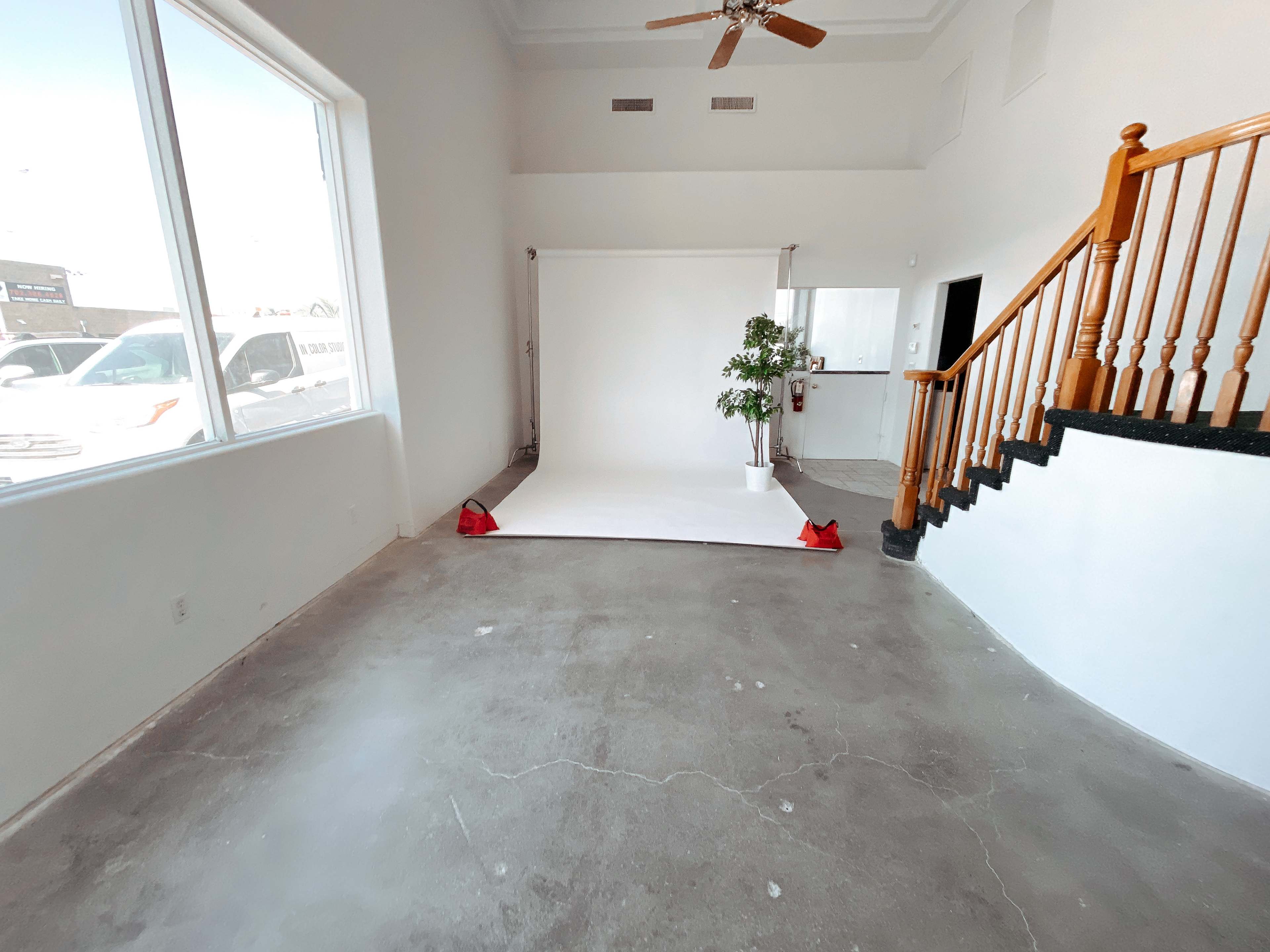 A spacious, brightly lit room with a white backdrop, a potted plant, and a staircase leading to a higher level.