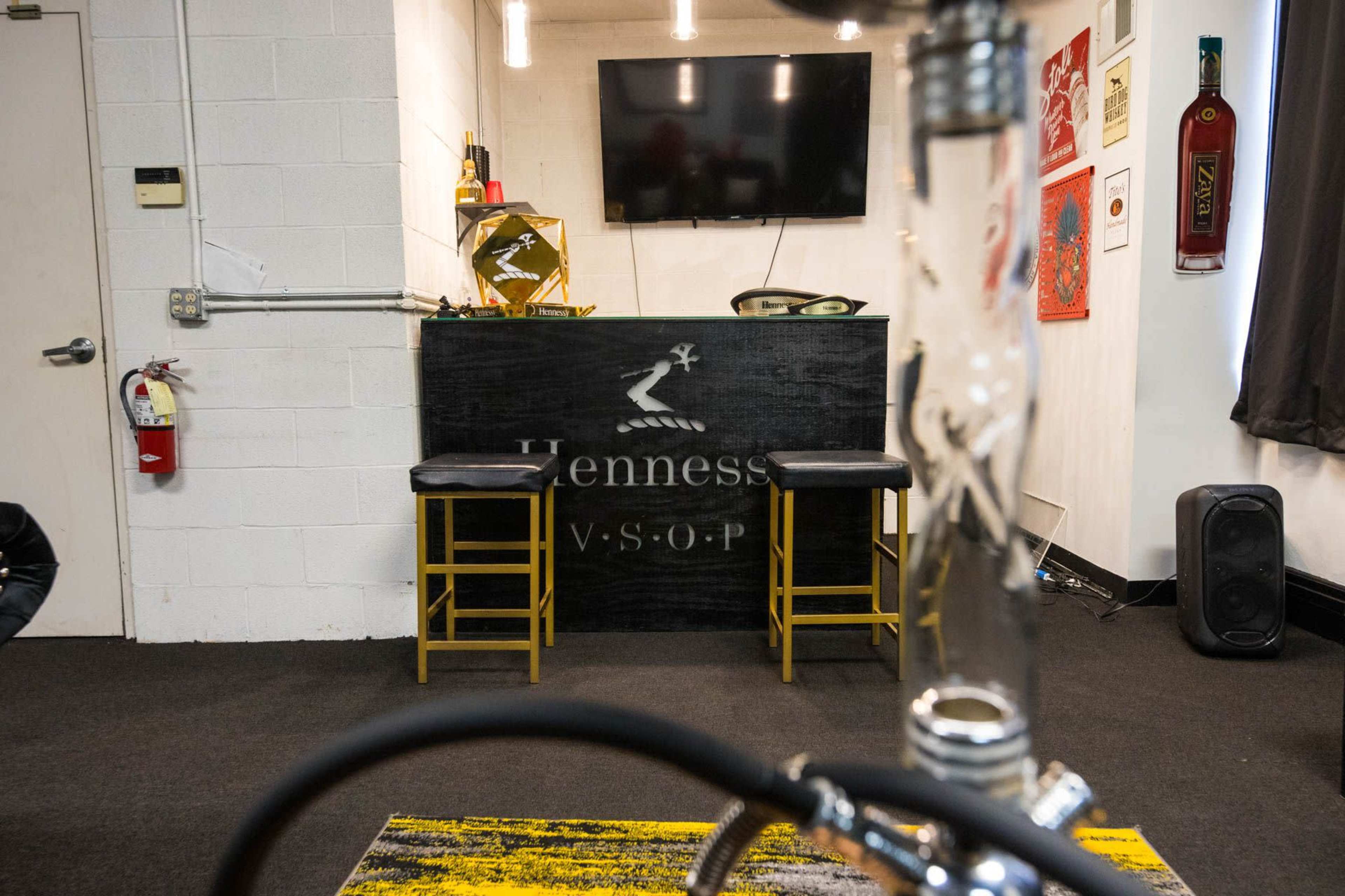 A bar area with two stools, a TV mounted on the wall, and a Hennessy VSOP logo prominently displayed on the bar counter.