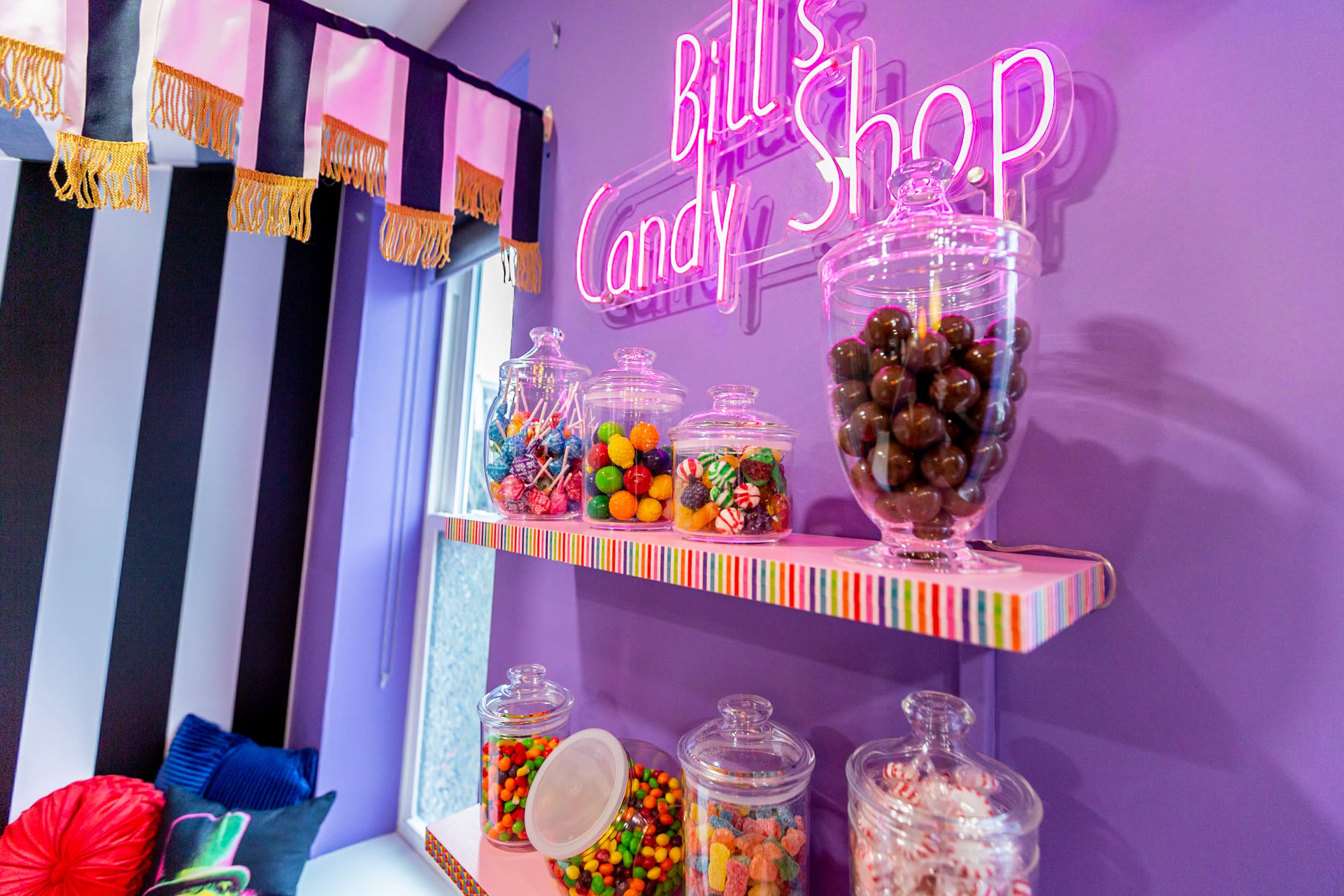 A colorful display of candy jars on shelves in a shop with a neon sign reading "Bill's Candy Shop."