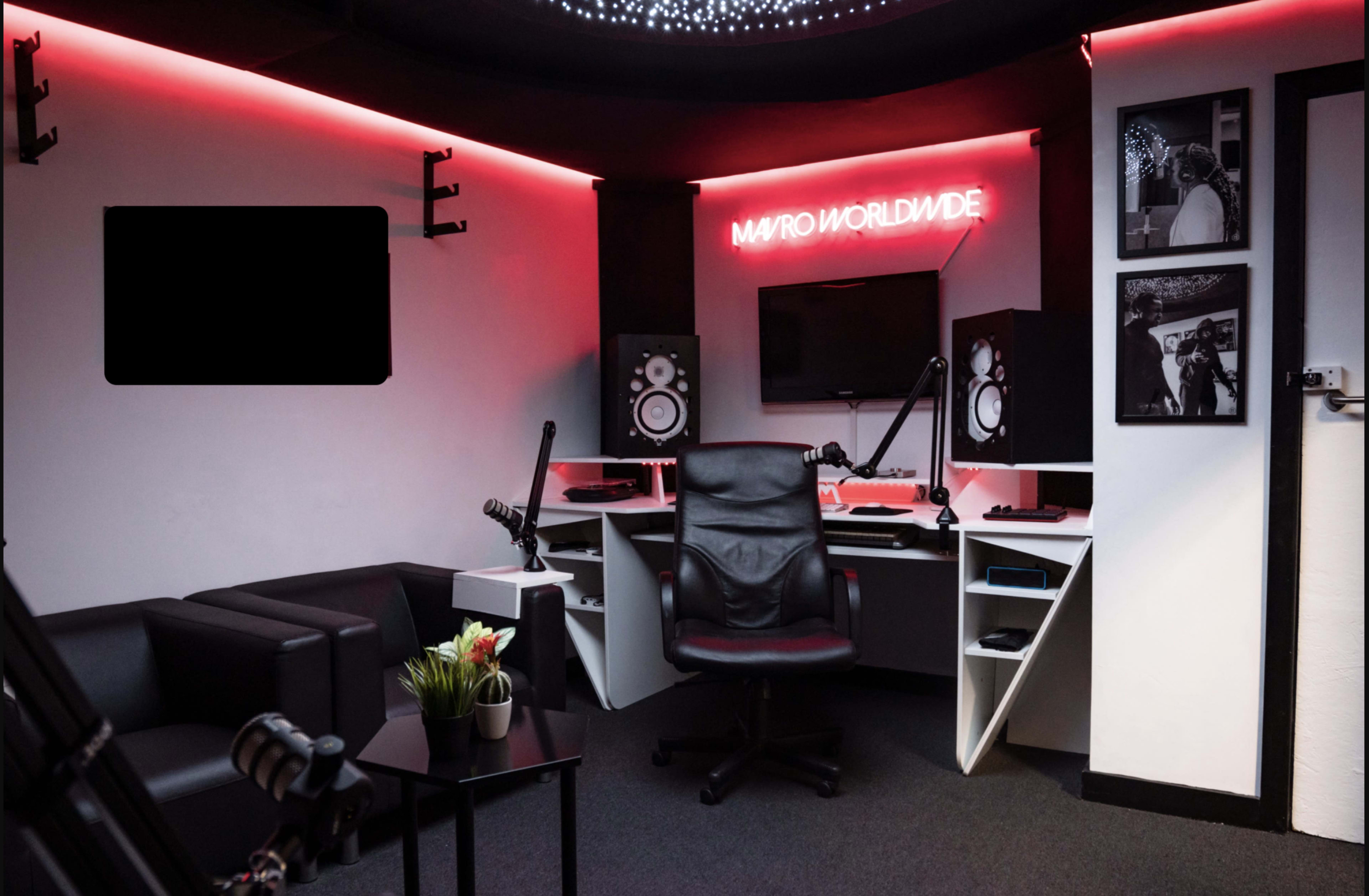 A modern recording studio with a black leather chair, a desk featuring audio equipment, and neon lighting displaying "MAYO WORLDWIDE."