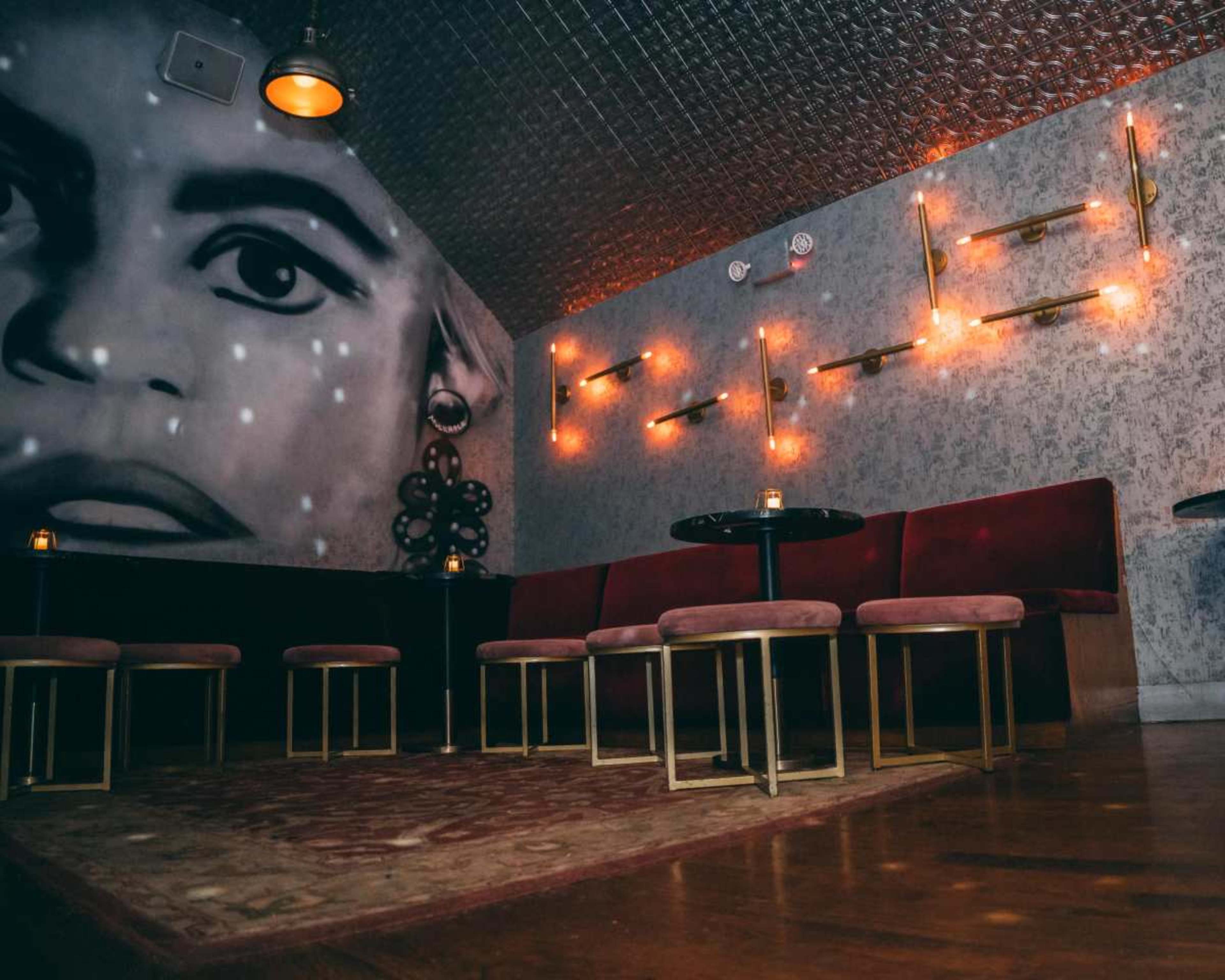 The image shows a dimly lit lounge area with plush seating and decorative wall art.