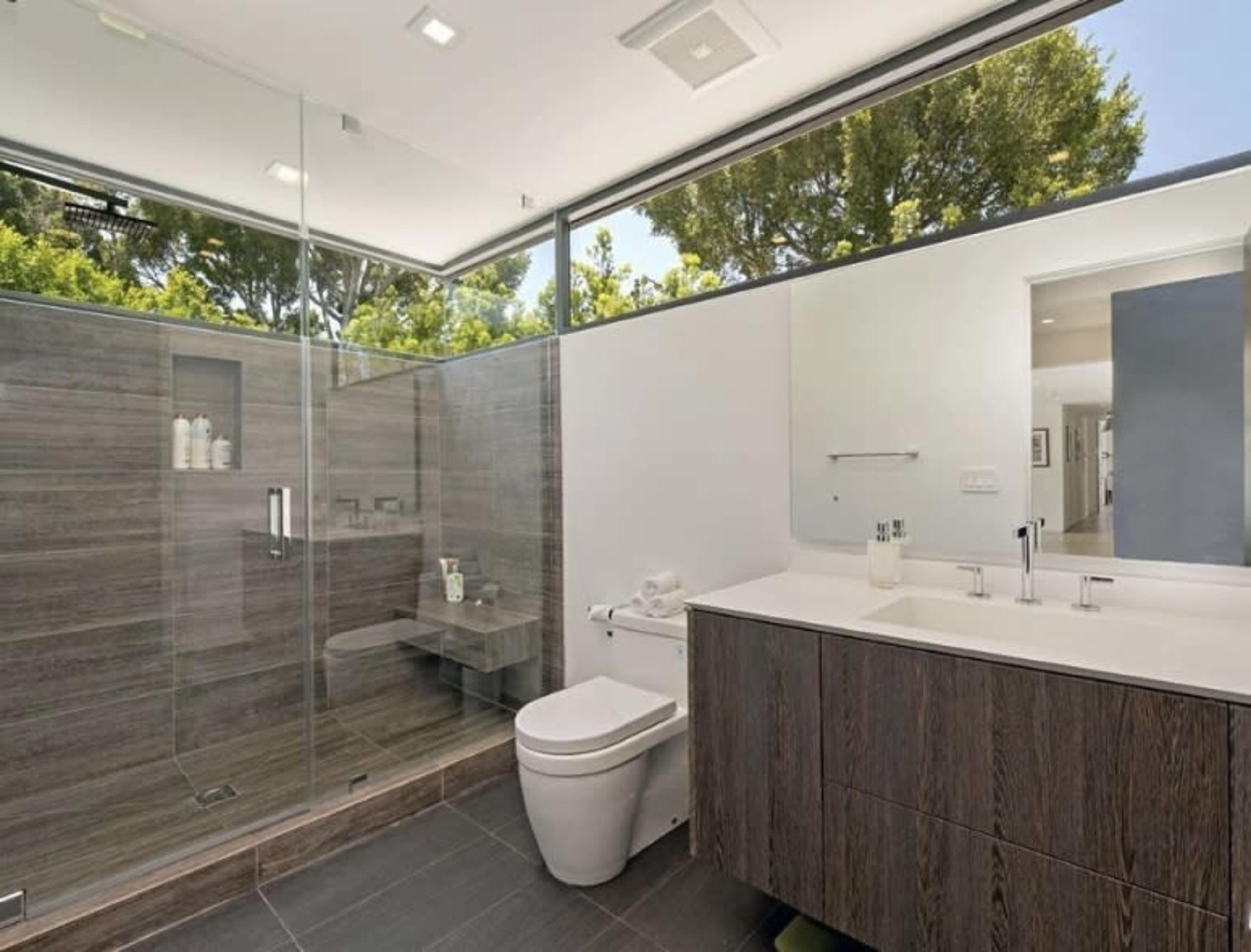 A modern bathroom with a glass shower, a toilet, and a double vanity with dark wood cabinetry.