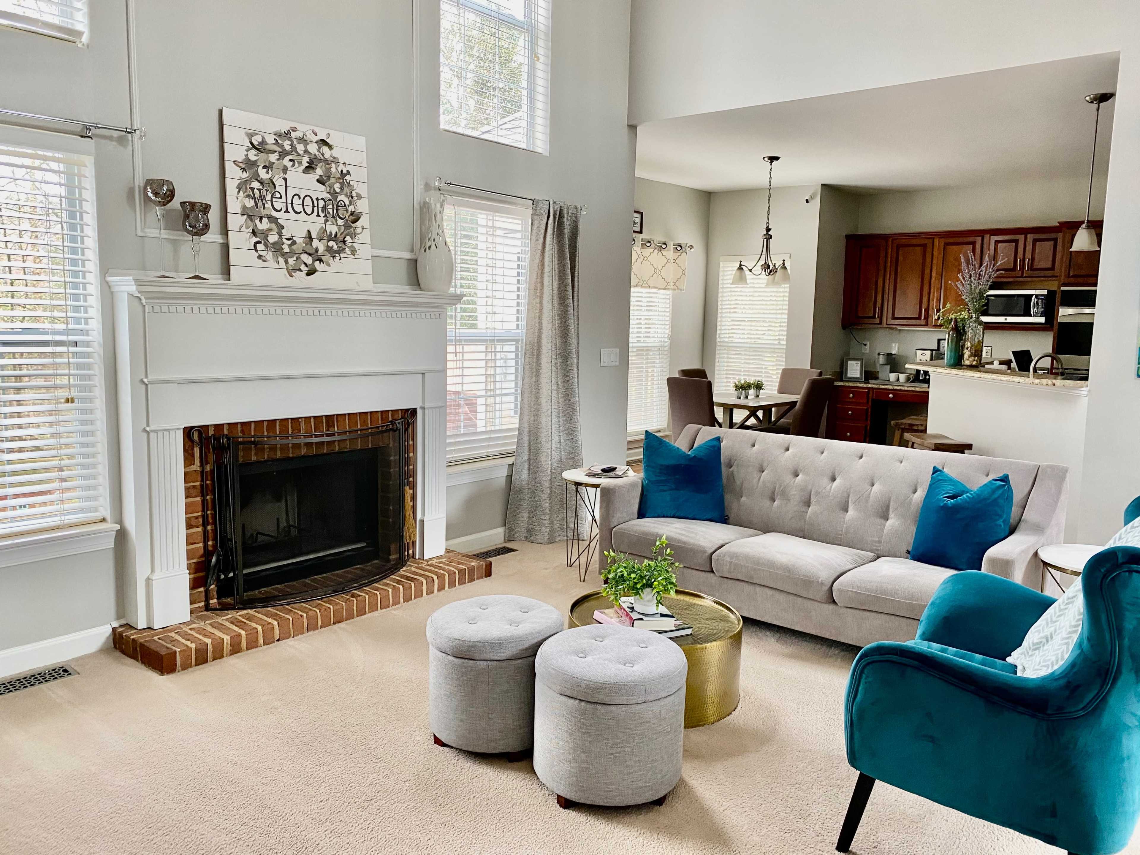 A modern living room features a gray sofa with blue pillows, a fireplace, and a small dining area visible in the background.