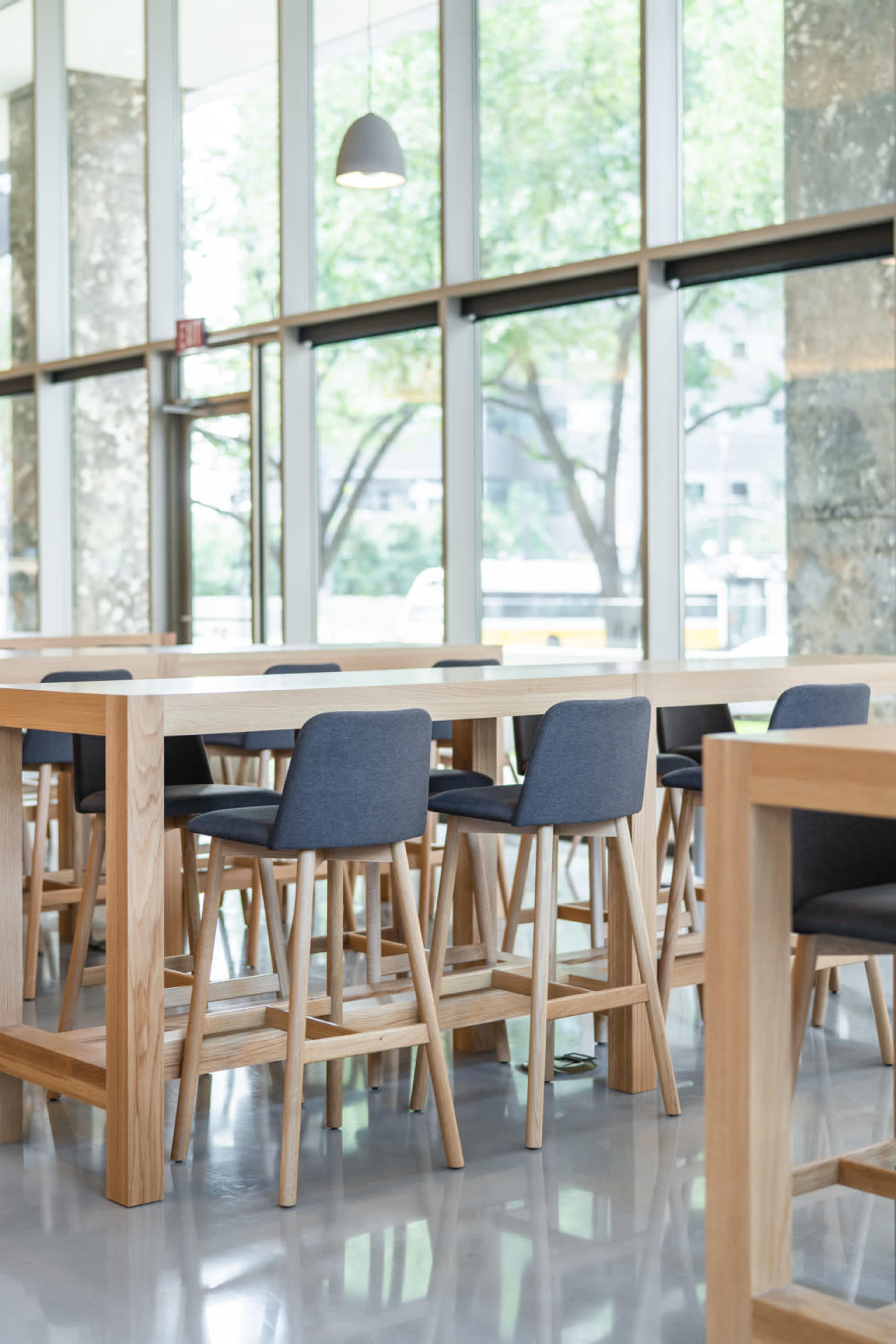 A modern dining area features wooden tables and high chairs set against large windows with views of trees outside.
