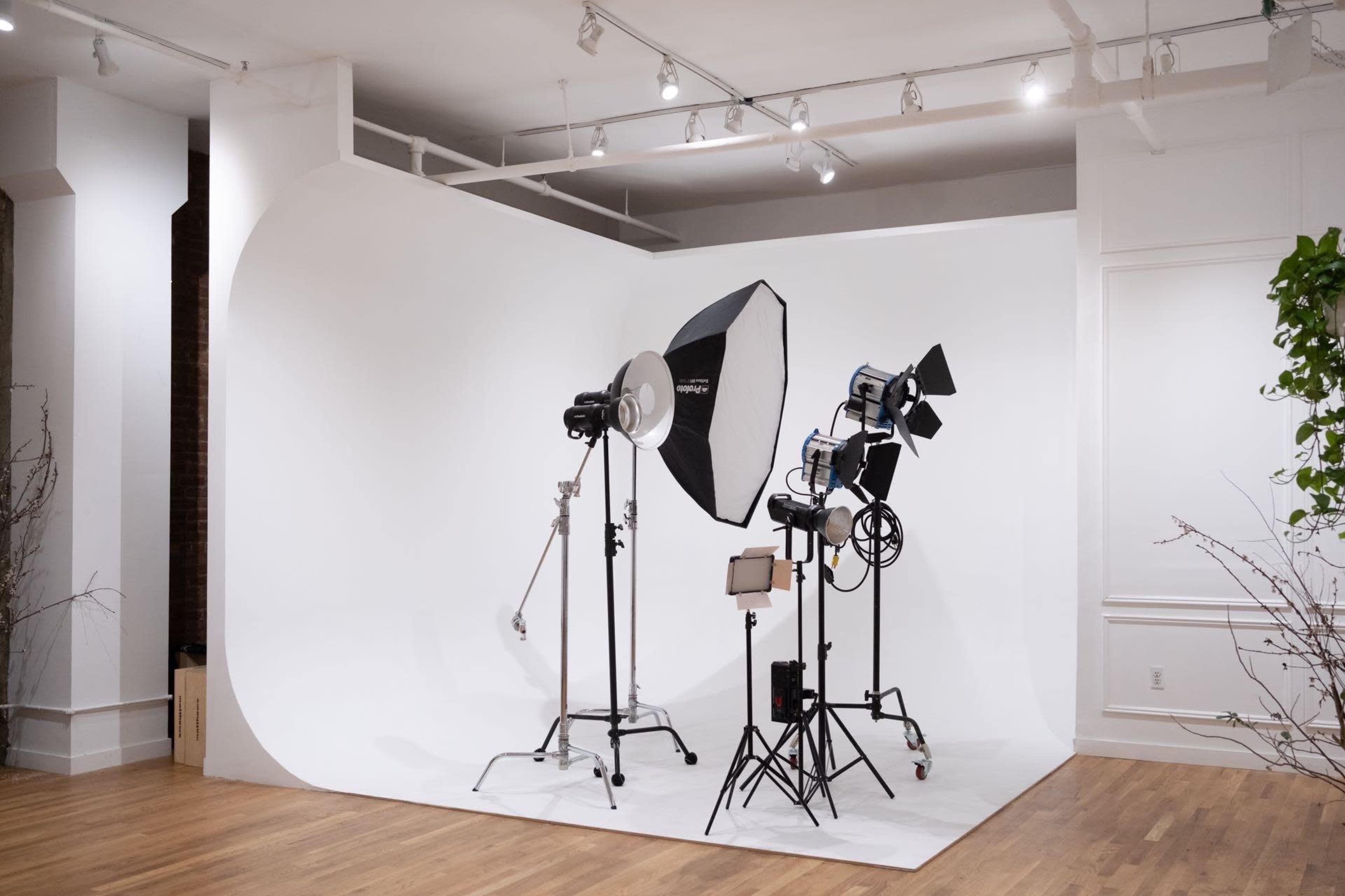 The image shows a photography studio setup featuring a curved white backdrop and multiple lighting equipment arranged neatly.