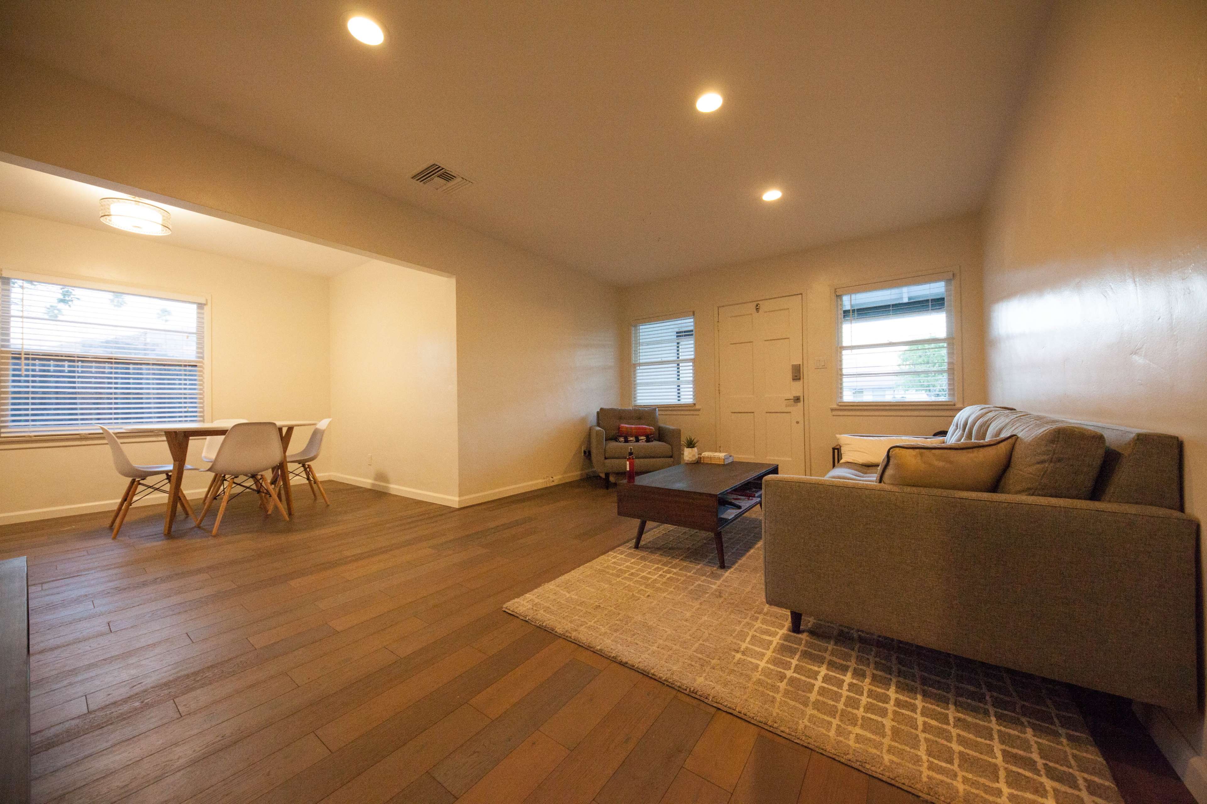 A light-colored living room features a sofa, a coffee table, and a dining area with a table and chairs.