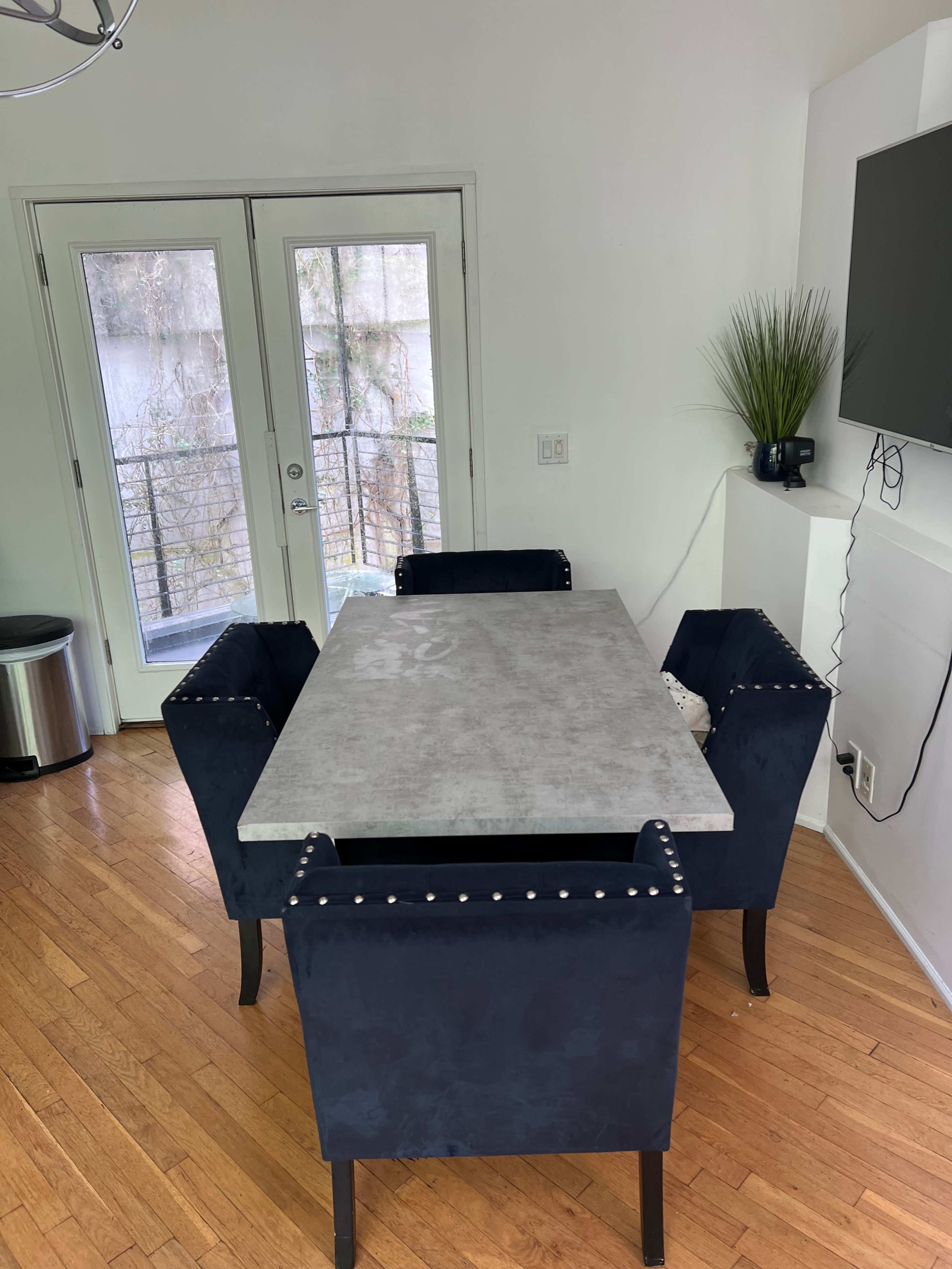 A rectangular table with a concrete top is surrounded by four navy blue velvet chairs in a well-lit room with large windows.
