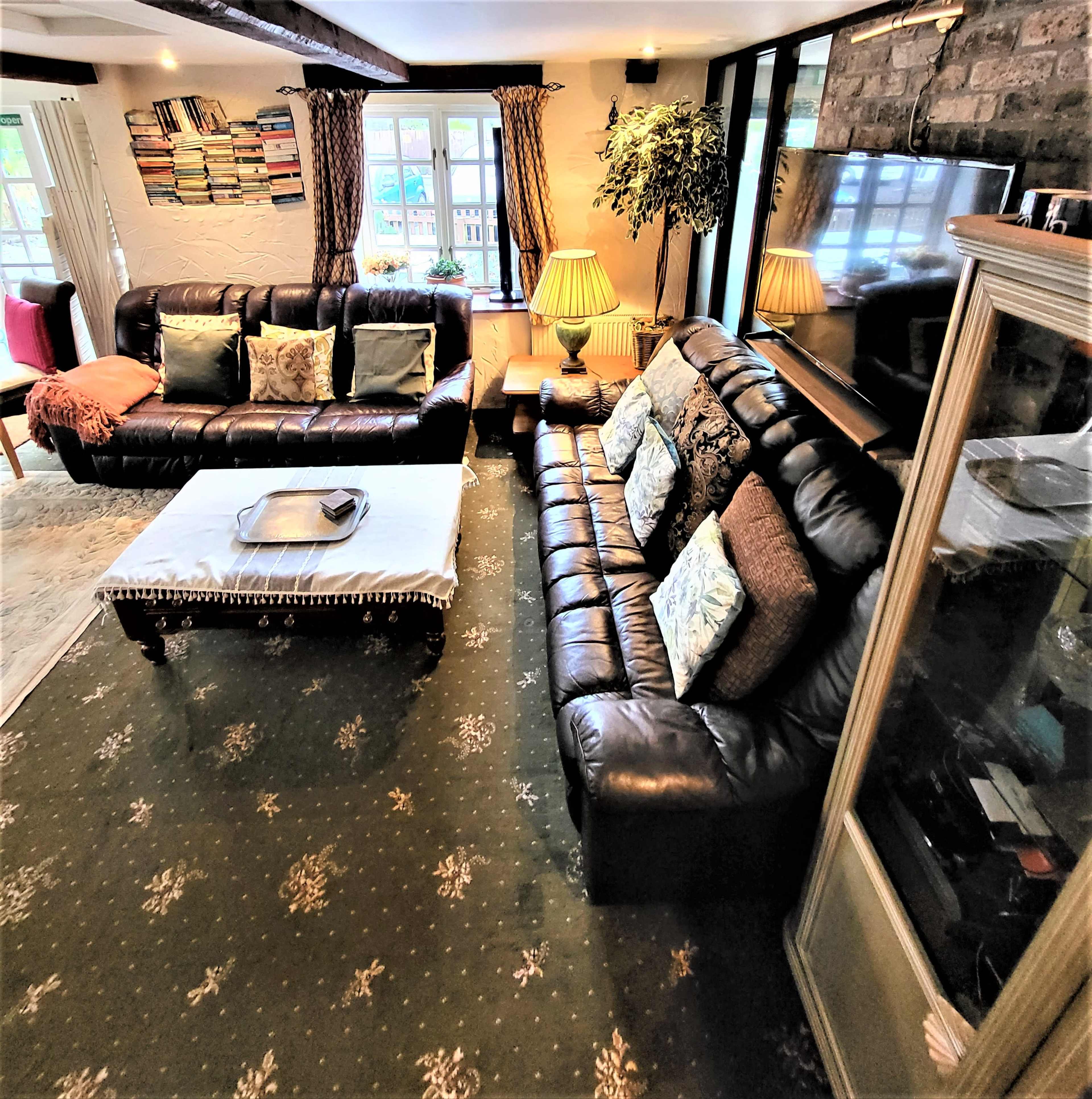 The image shows a cozy living room with dark leather sofas, a large television, a bookshelf, and a decorative glass cabinet.