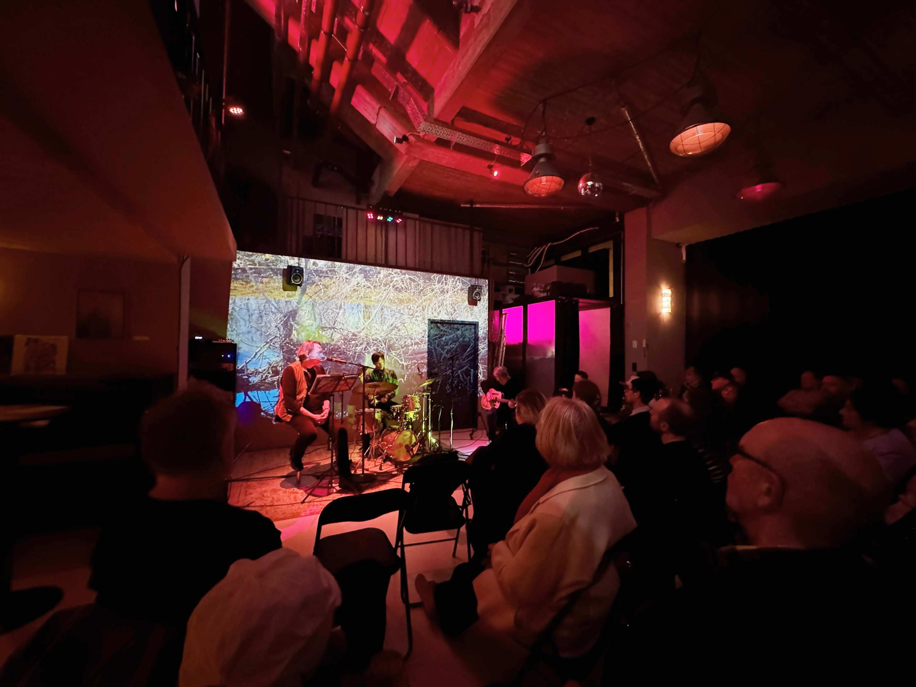 A band performs on stage in front of an audience, with vibrant lighting and a projected background.