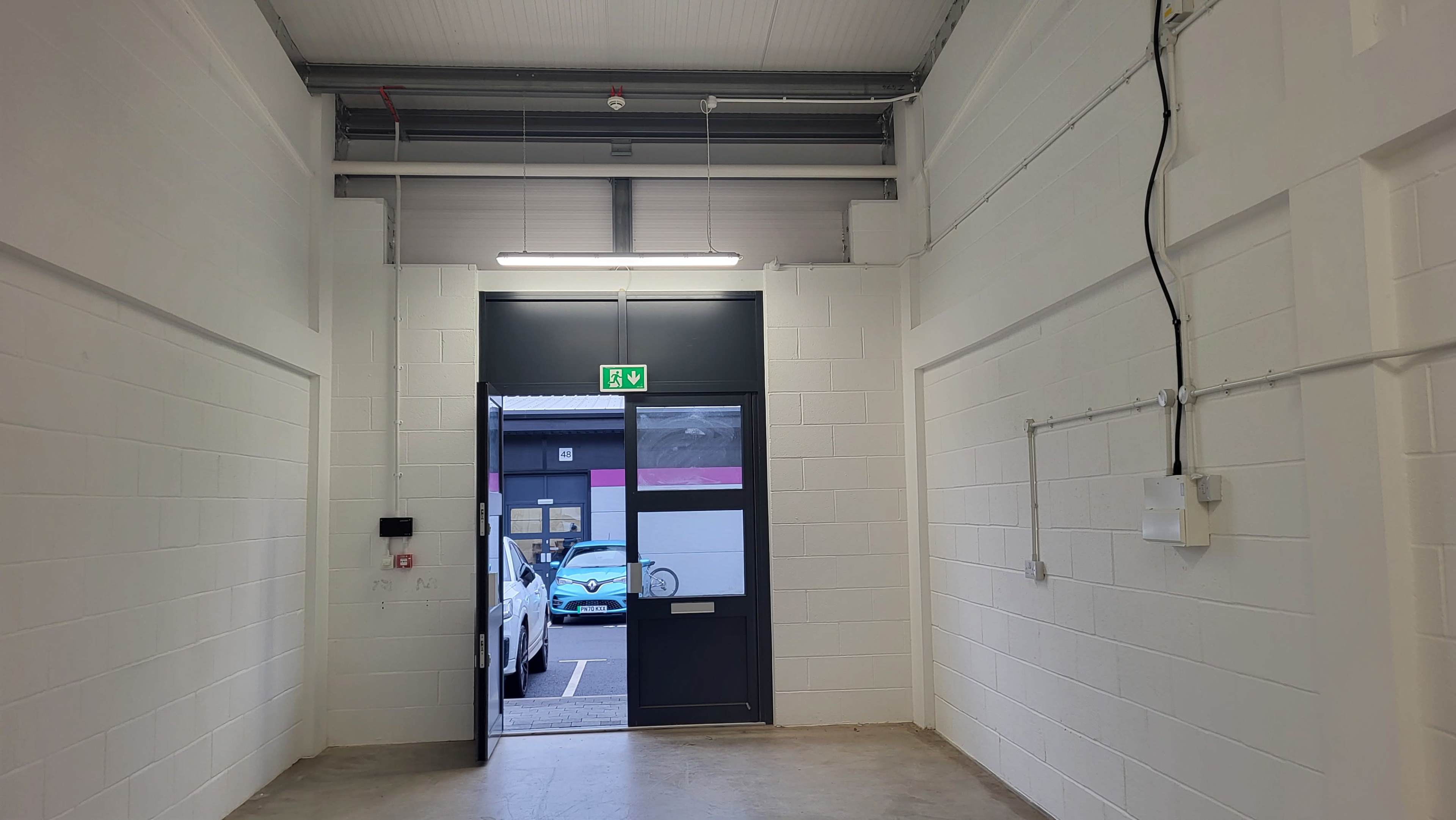 A view of an empty corridor leading to a door with a glass panel, providing a glimpse of a parking area outside.