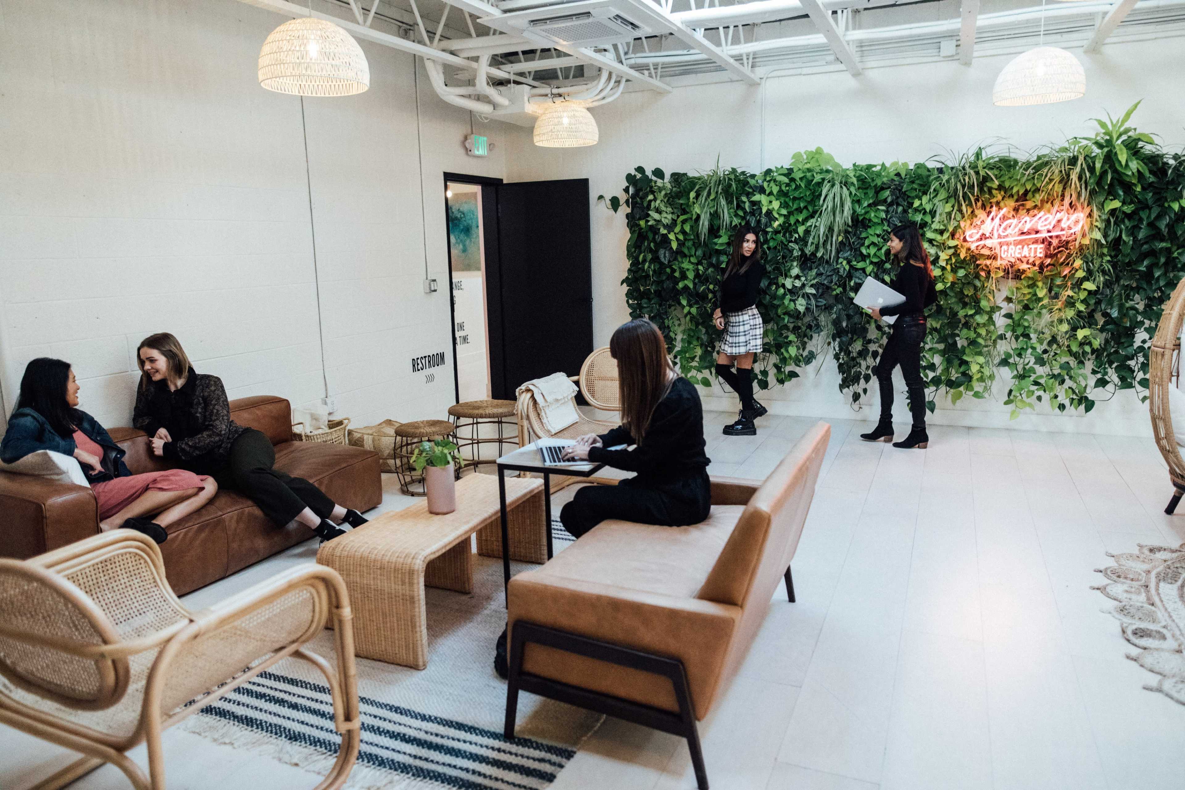 A modern lounge area with plants, seating arrangements, and people engaged in conversation and work activities.