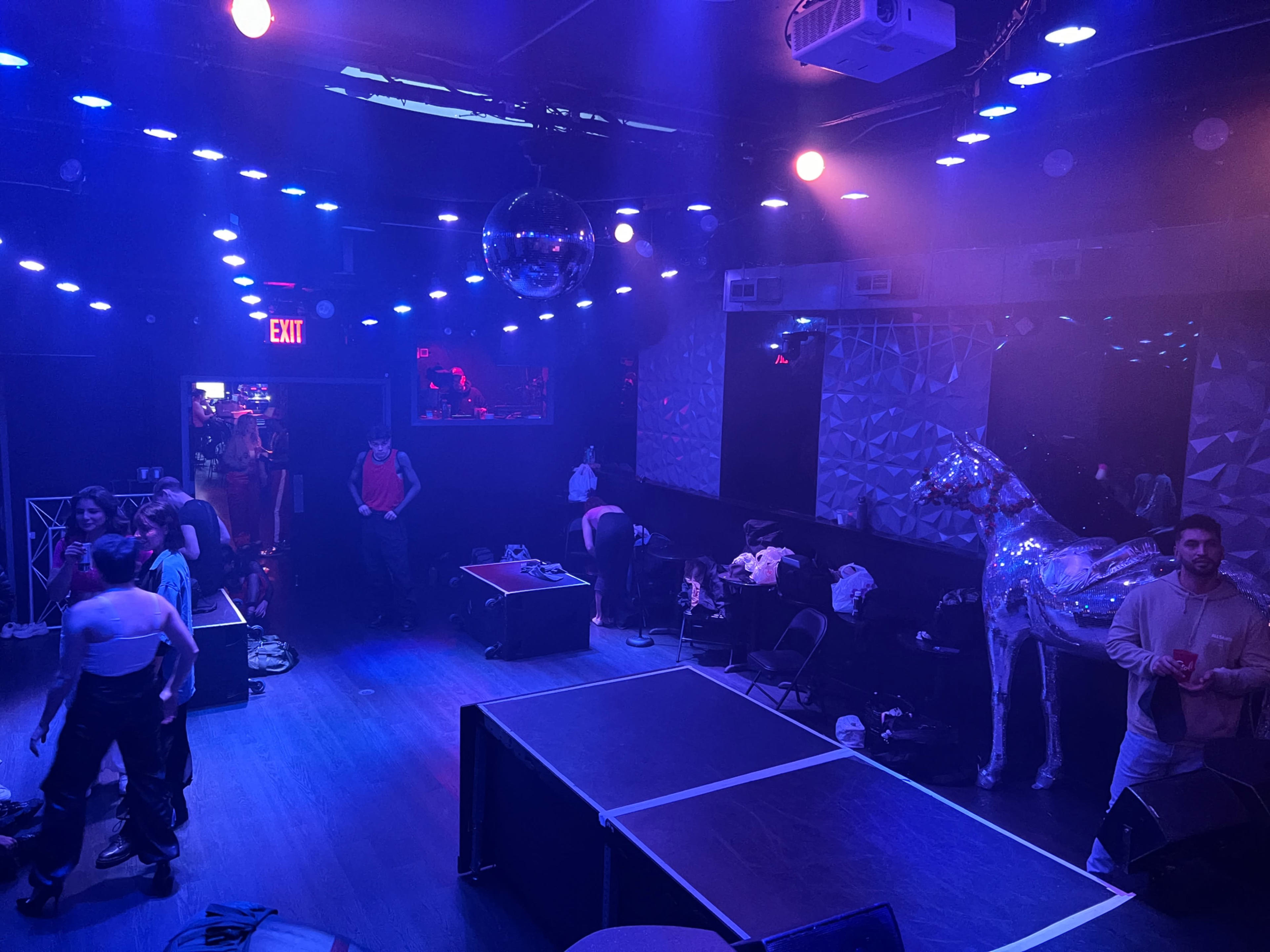 A dimly lit room with disco lights, featuring a mirrored wall and a shiny horse sculpture, where people are setting up for an event.