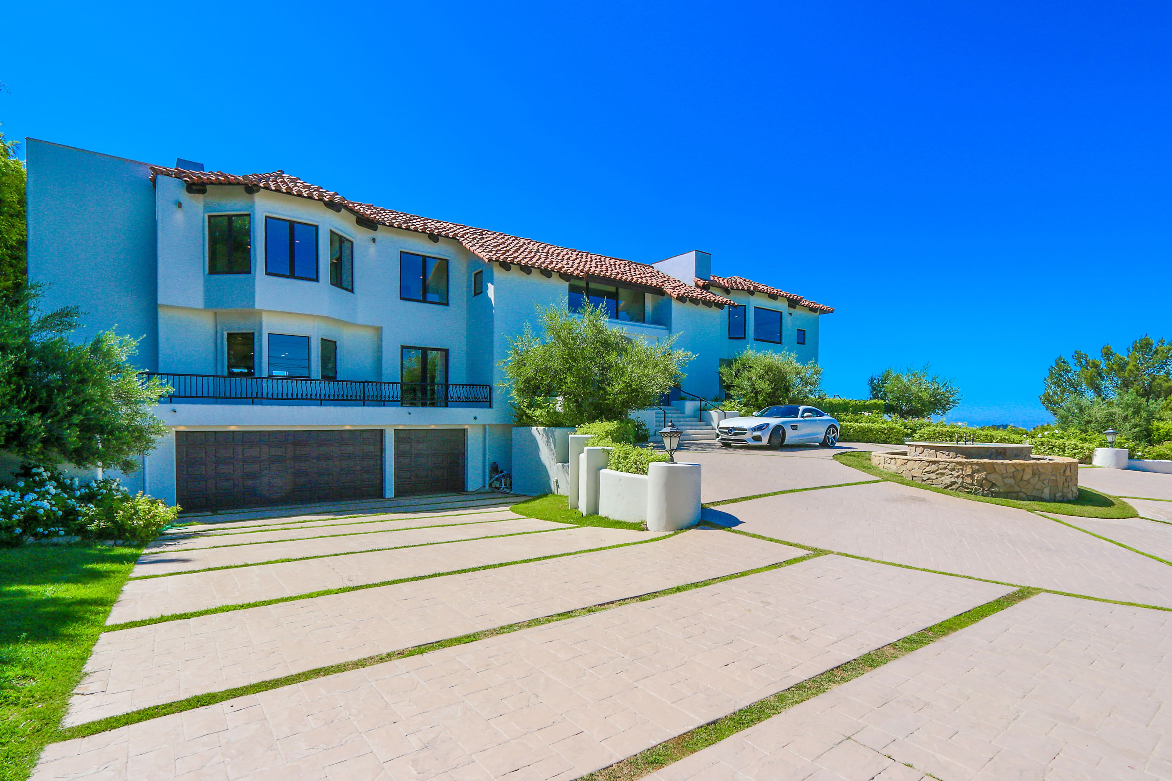 A modern two-story house with a tile roof, large windows, and a spacious driveway leads up to it.
