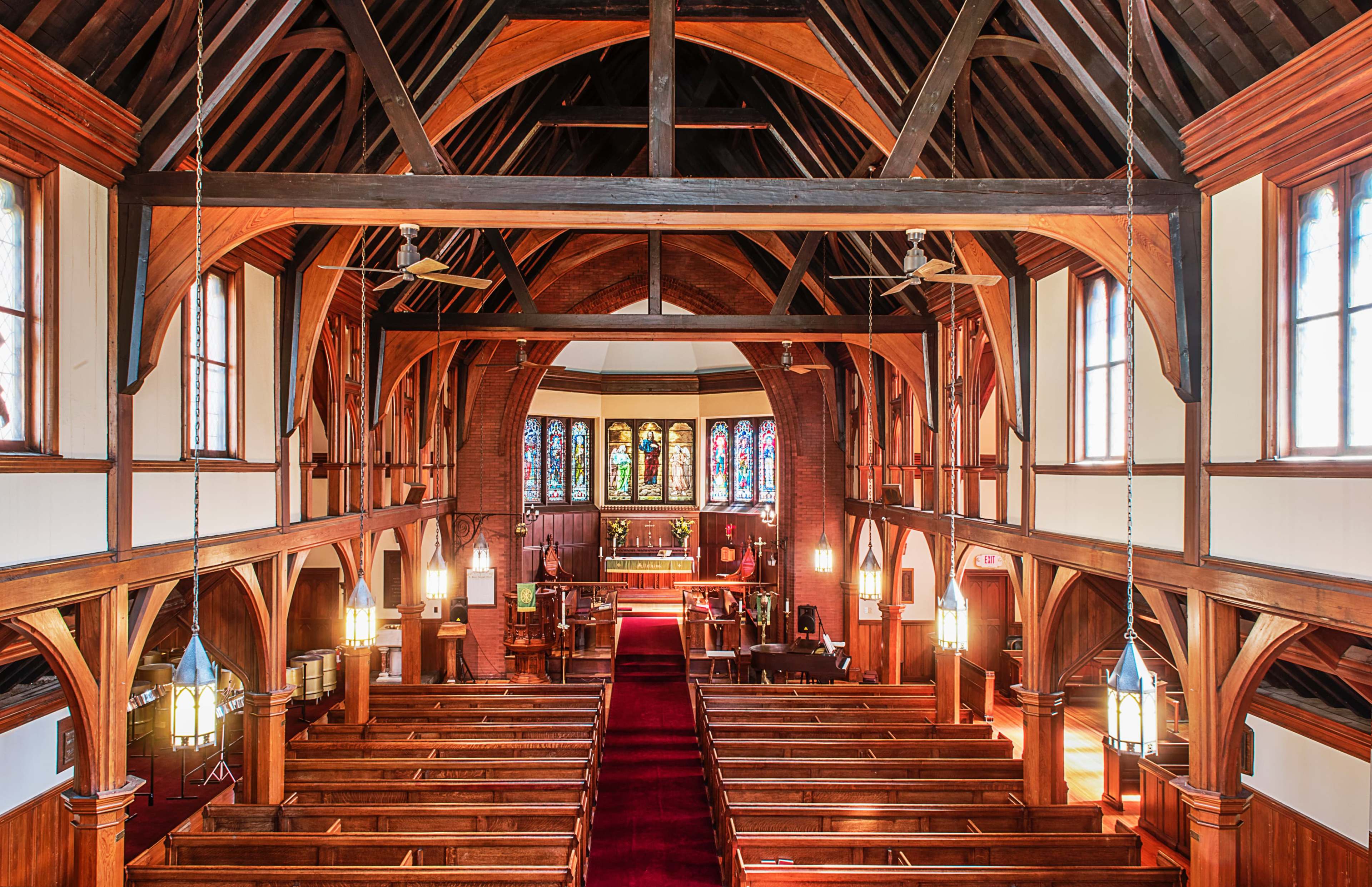 An interior view of a church featuring wooden beams, stained glass windows, and rows of pews leading to an altar.