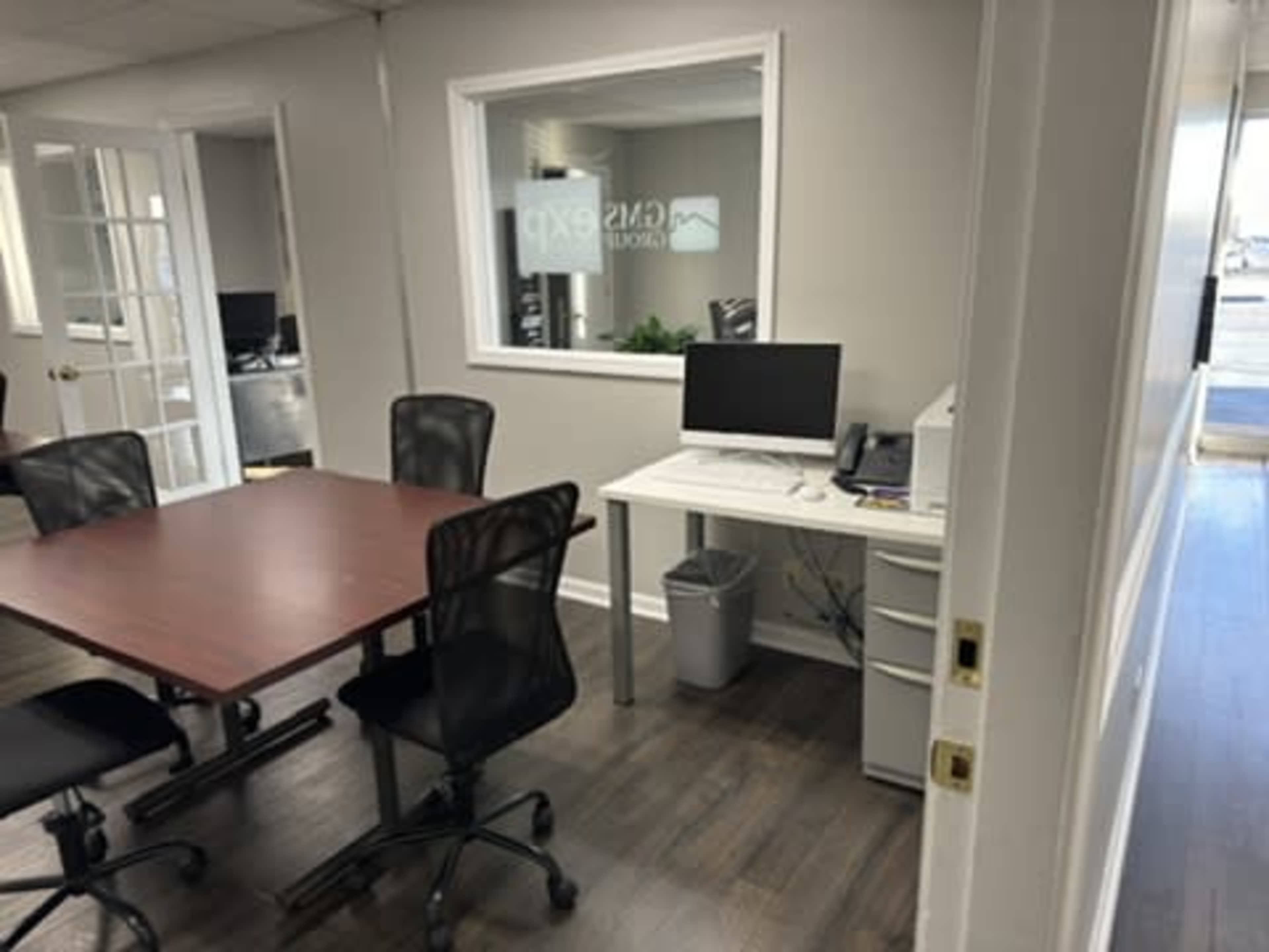 A modern office space with a desk, a computer, and several black chairs arranged around a central table.