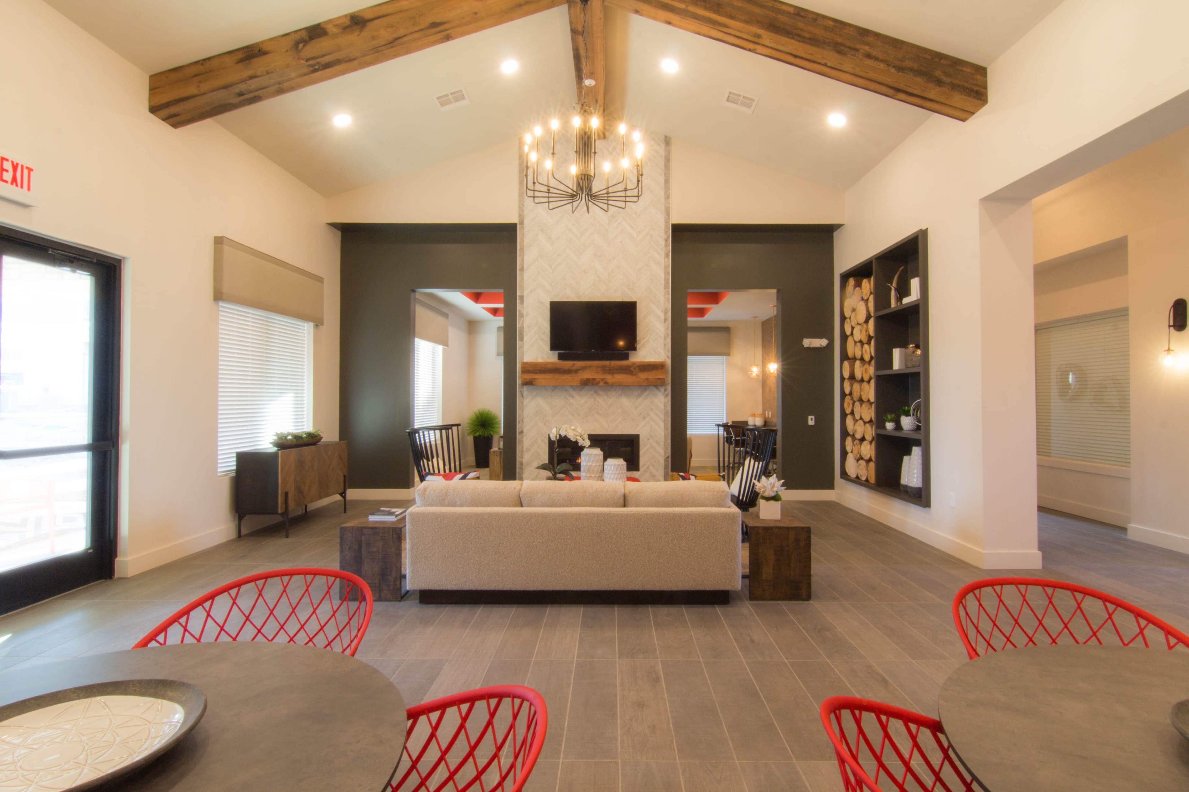 A modern living room with a high ceiling, wooden beams, a sofa, and a fireplace, flanked by windows and two armchairs.