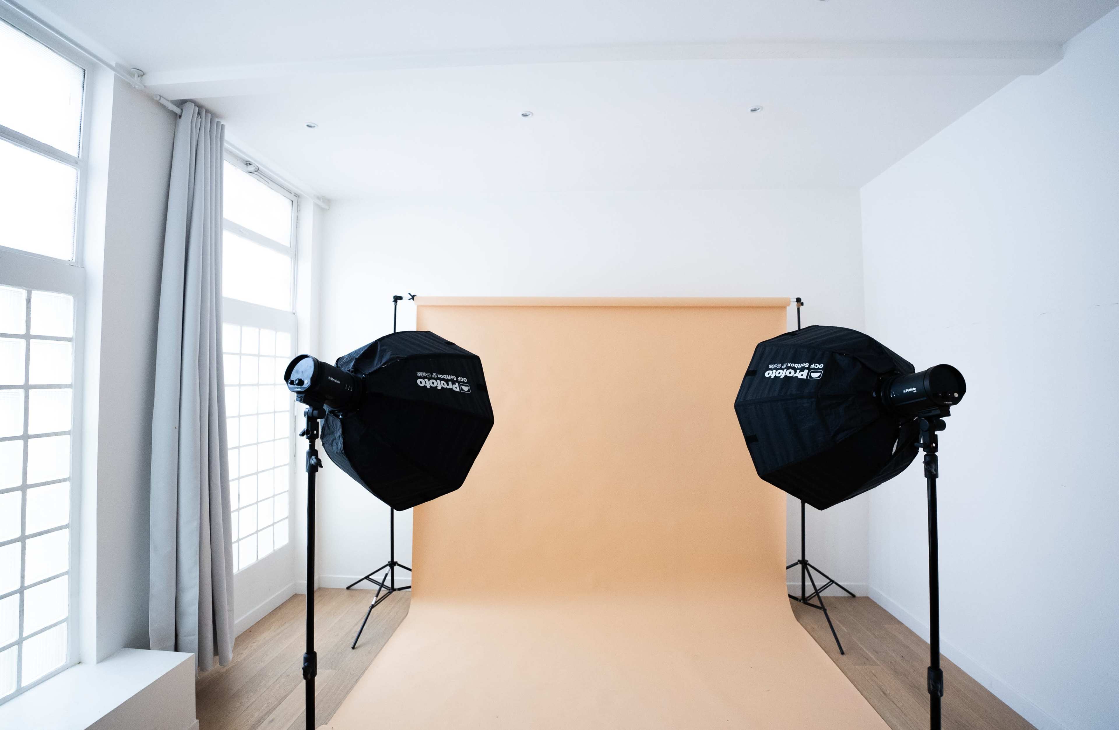 A photography studio with two softbox lights positioned in front of a plain orange backdrop.
