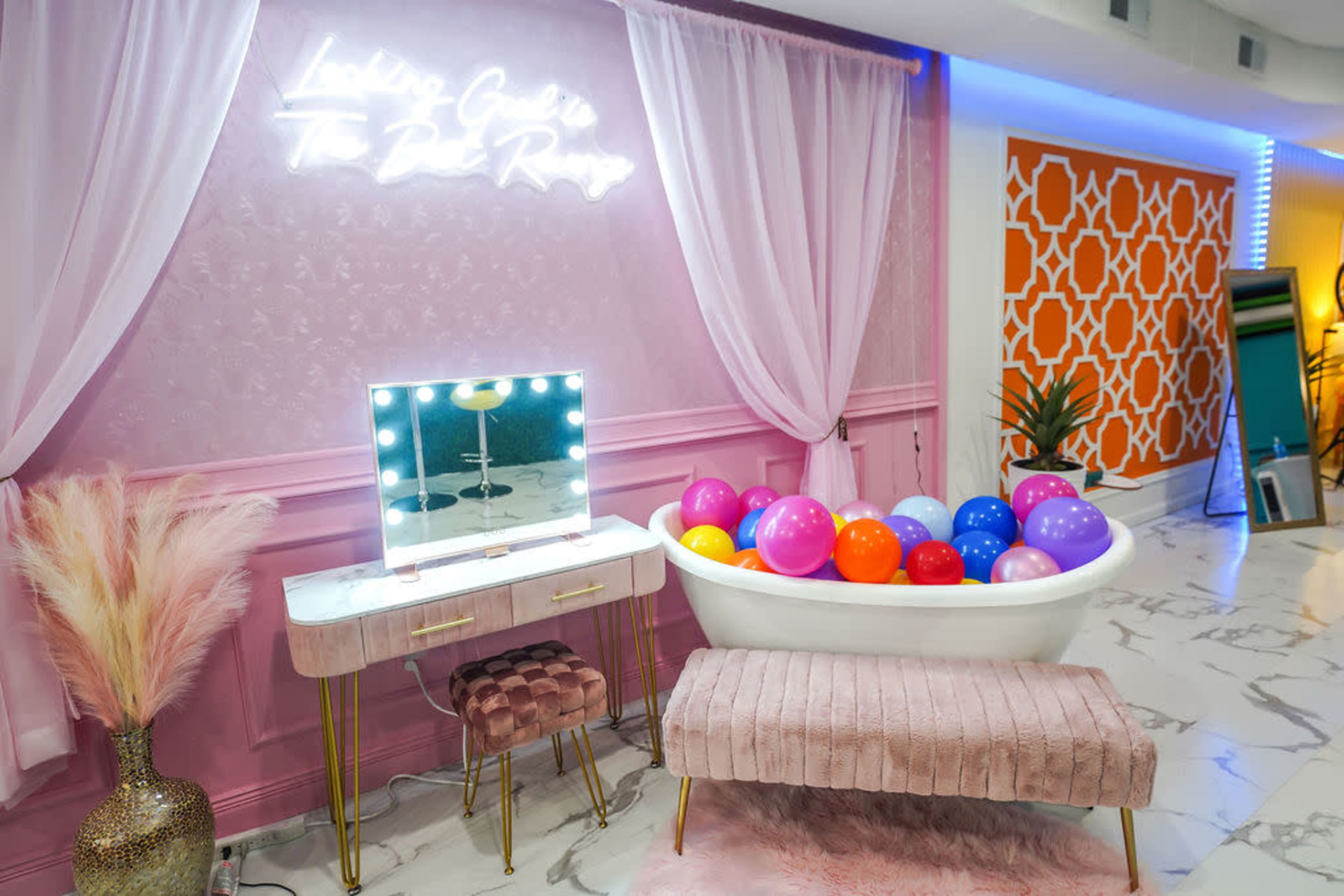 A stylish indoor space featuring a bathtub filled with colorful balls, accompanied by a vanity mirror and a plush bench against a decorative wall with soft lighting.