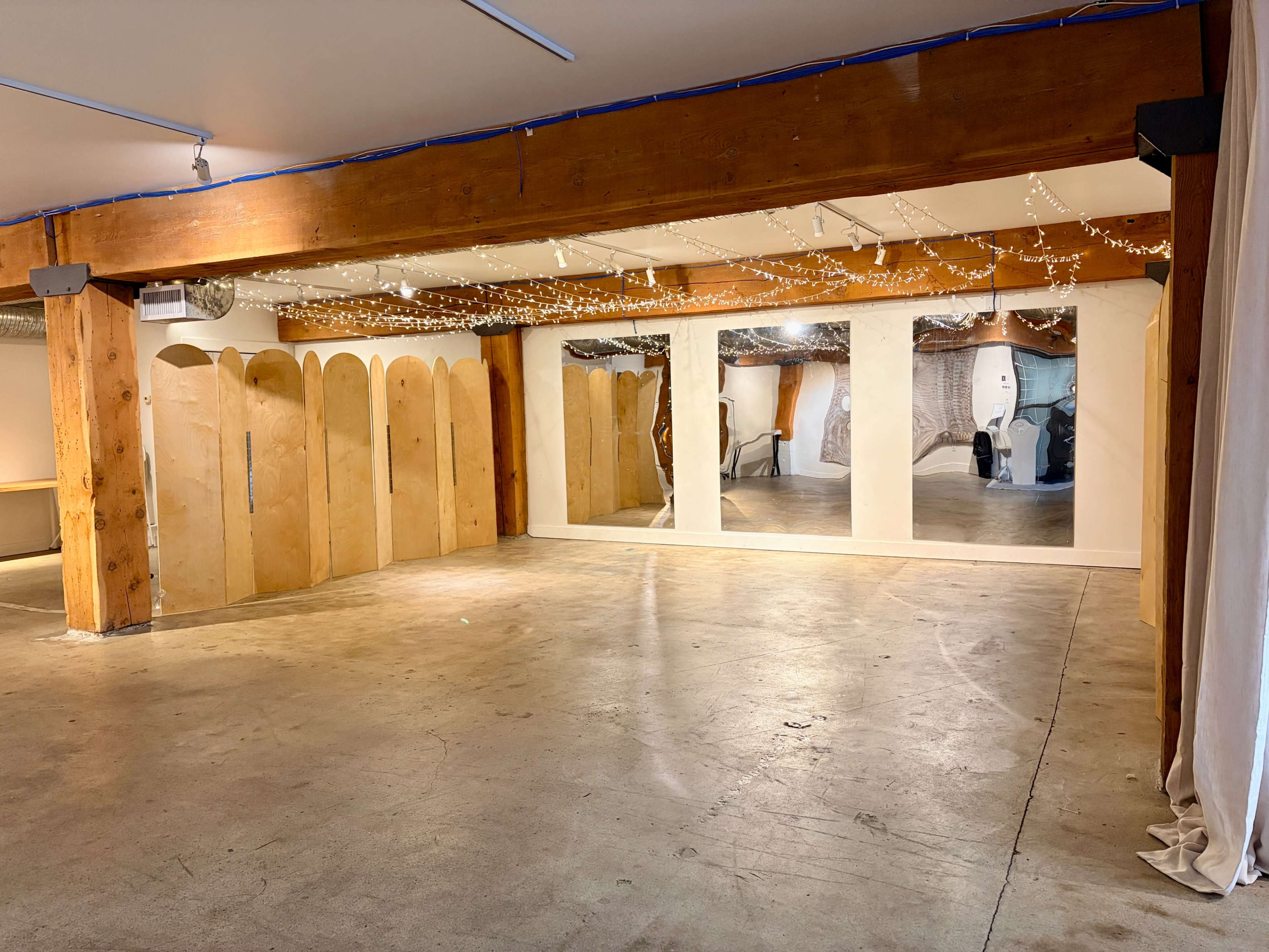 The image shows an empty room with wooden beams, decorative lights, and mirrored panels against the walls.
