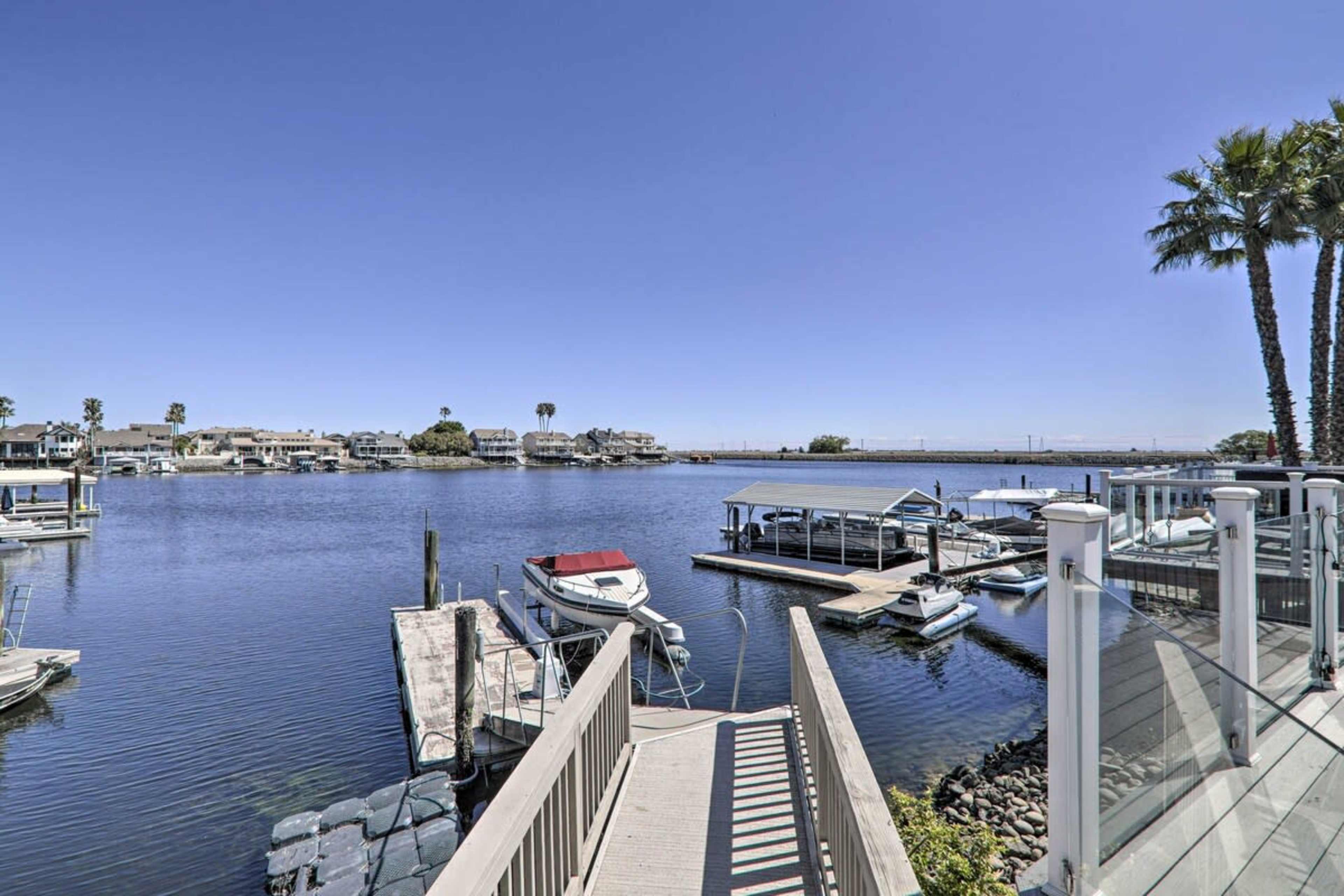 A marina with several boats docked beside a calm waterway, framed by palm trees under a clear blue sky.