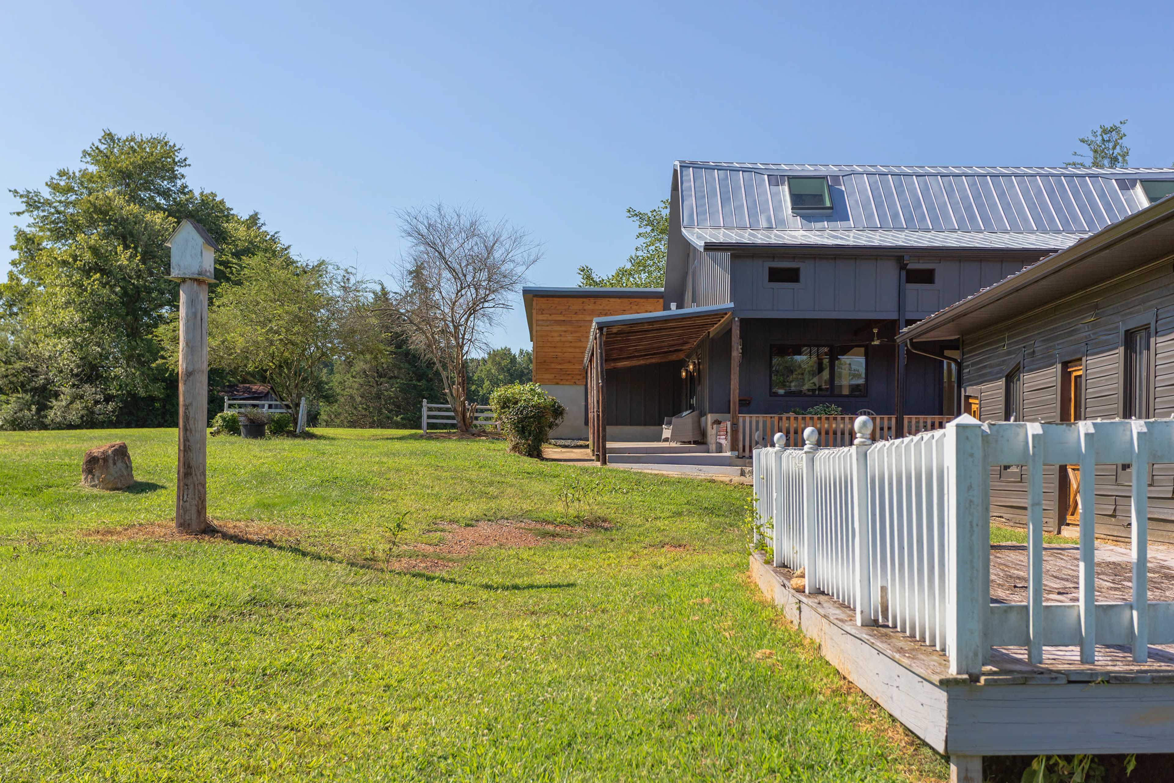 A wooden post stands in a grassy area next to a modern, two-story house with a metal roof and a deck.