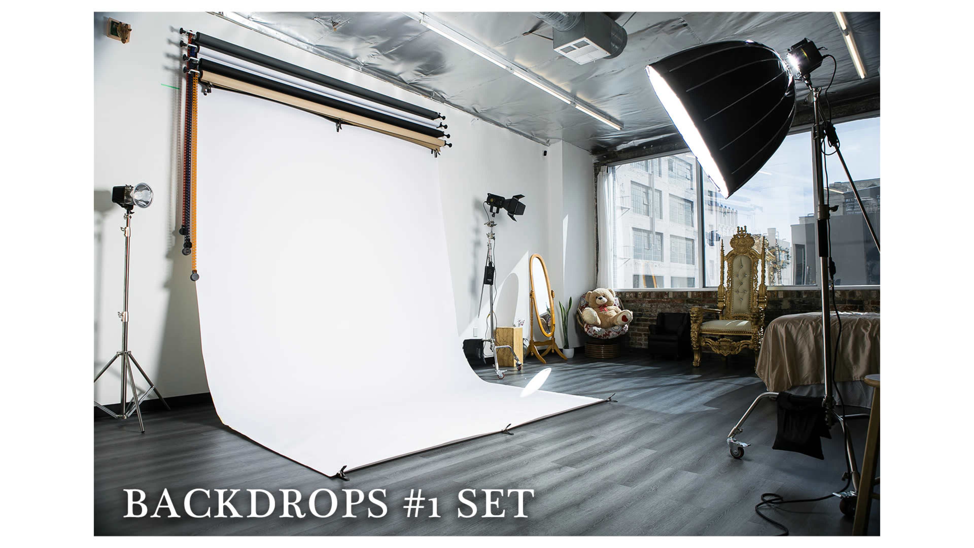 The image shows a photography studio with a white backdrop, lighting equipment, and various props arranged in a well-lit space.