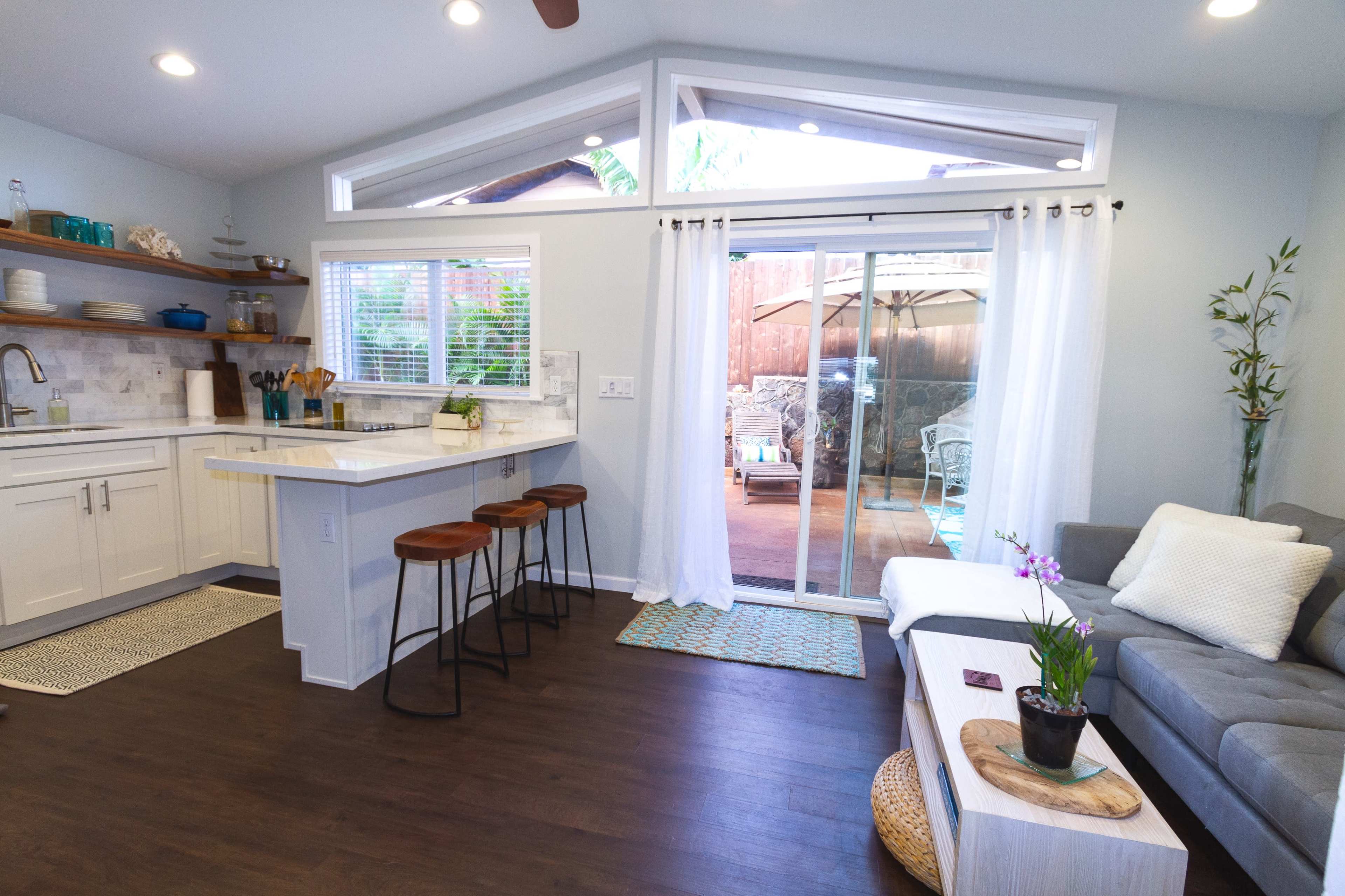 A modern kitchen and living area with a bar space, sliding glass doors leading to an outdoor patio, and a small potted plant on a coffee table.