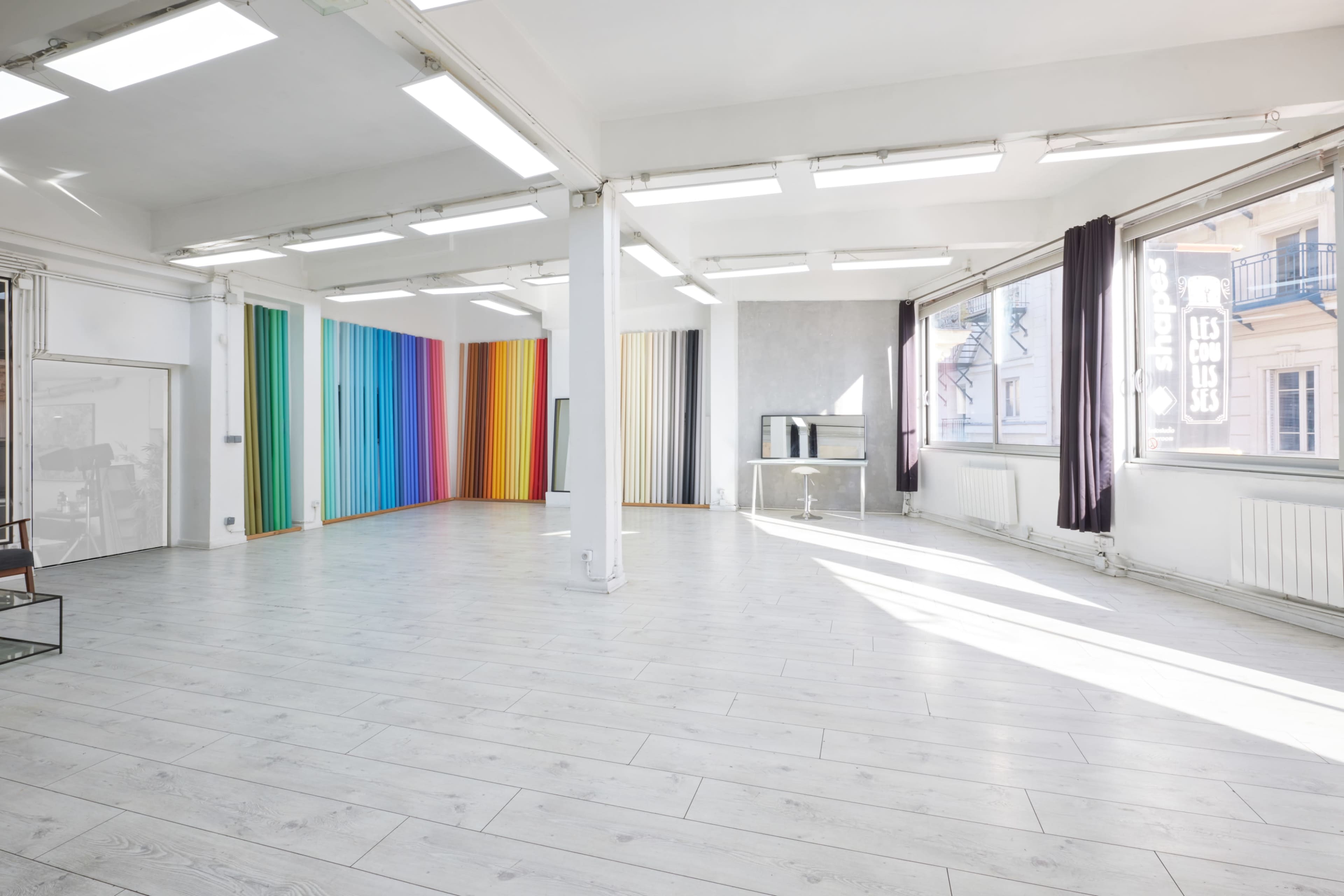 The image shows a spacious, empty room with a colorful striped wall and large windows allowing natural light to fill the space.