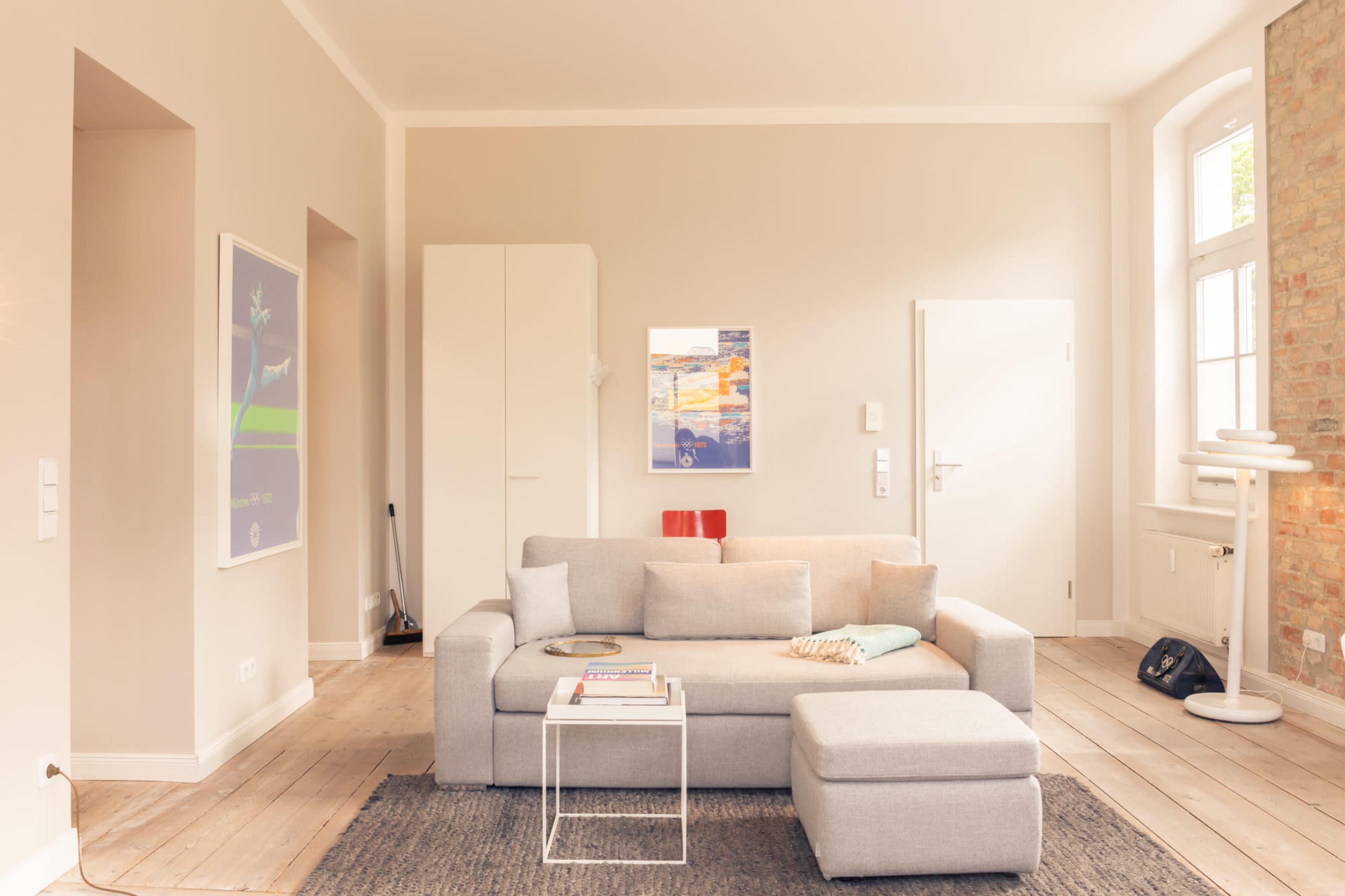 A modern living room features a gray sectional sofa, a light rug, and a minimalist table, with large windows allowing natural light to fill the space.